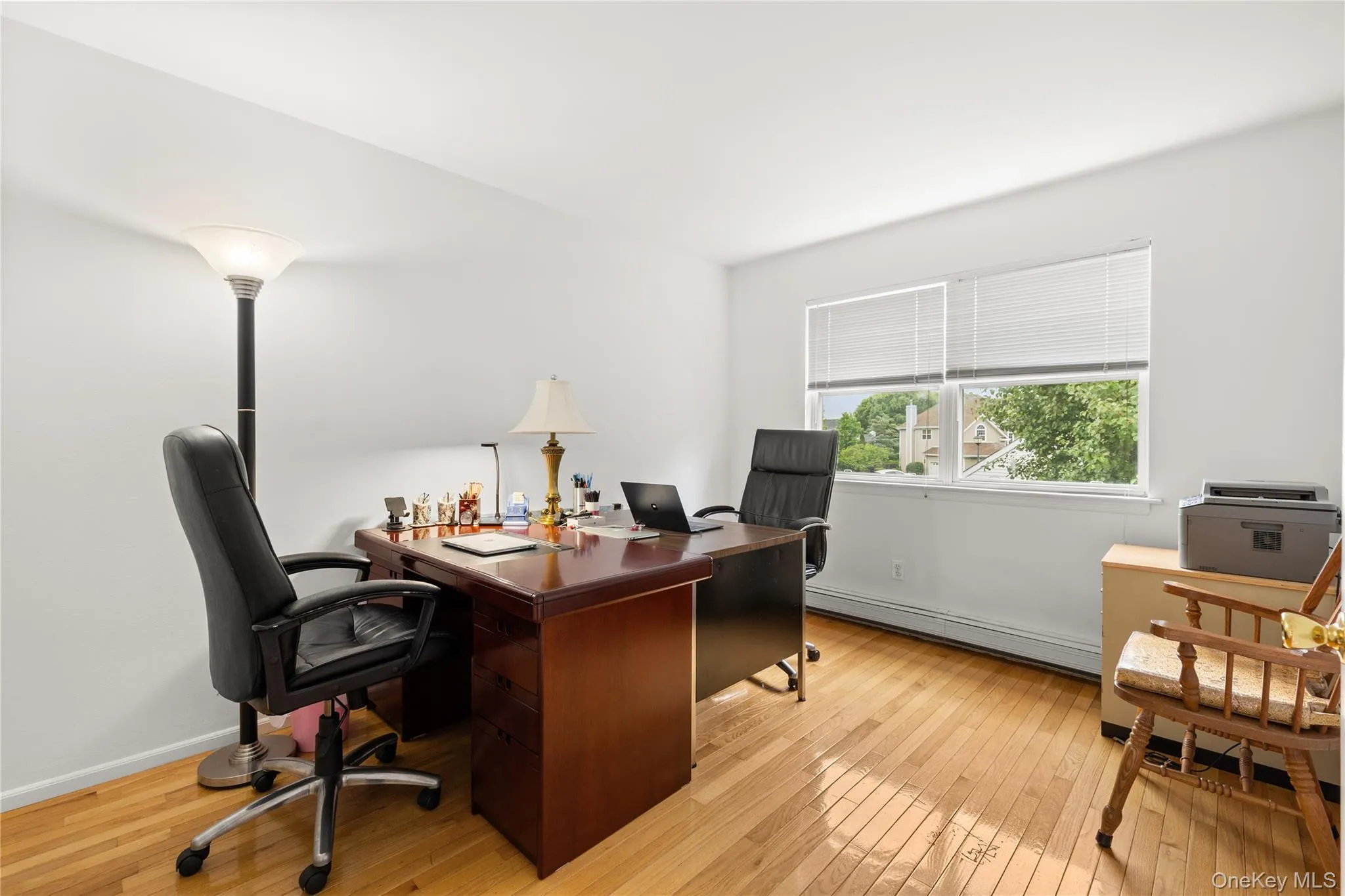 Bright interior room featuring hardwood flooring, white walls, and a large window with blinds Bright interior room featuring hardwood flooring, white walls, and a large window with blinds