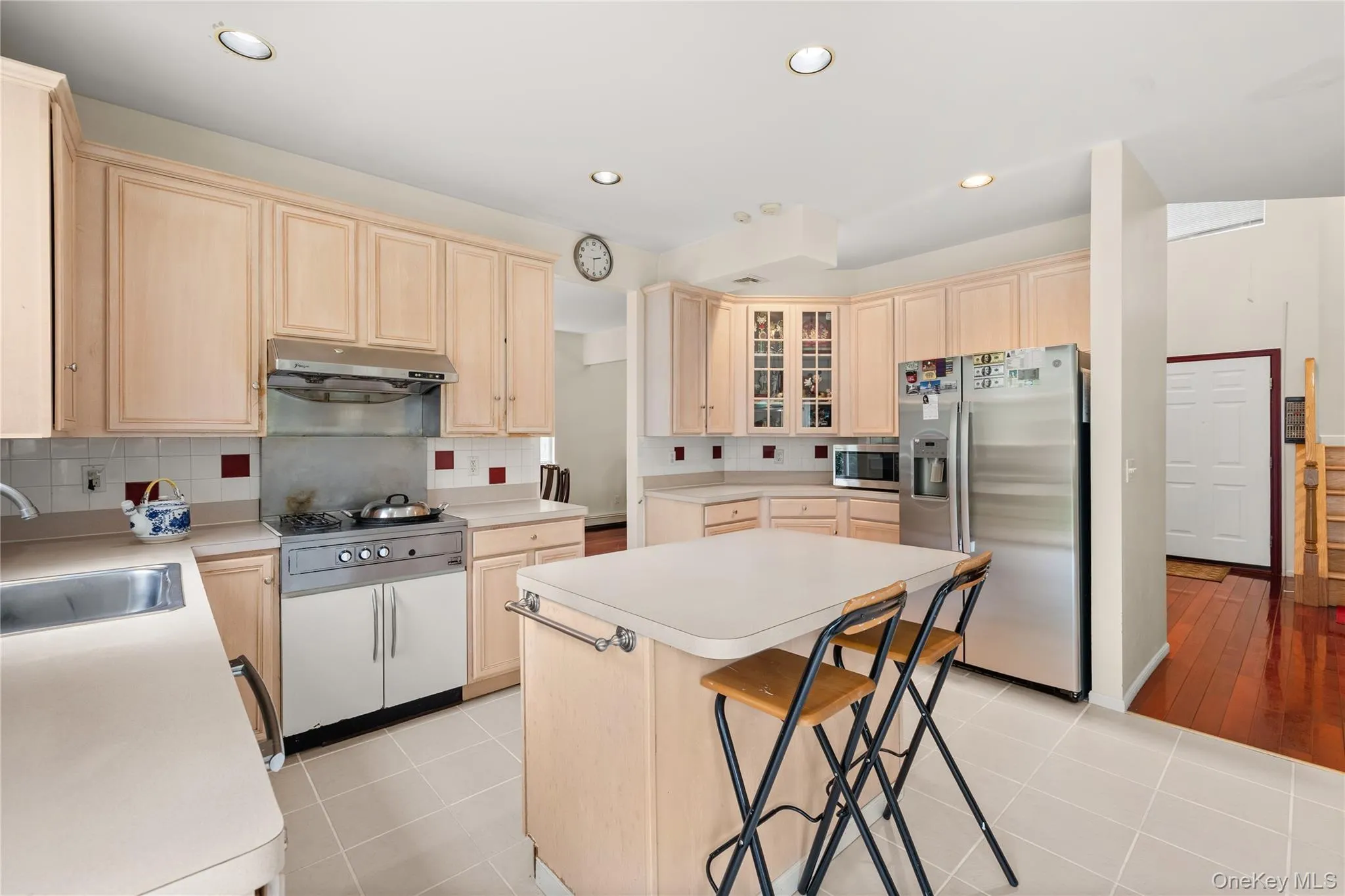 Kitchen featuring light wood-finish cabinetry, a central island, recessed lighting, white tiled flooring, and stainless steel appliances Kitchen featuring light wood-finish cabinetry, a central island, recessed lighting, white tiled flooring, and stainless steel appliances