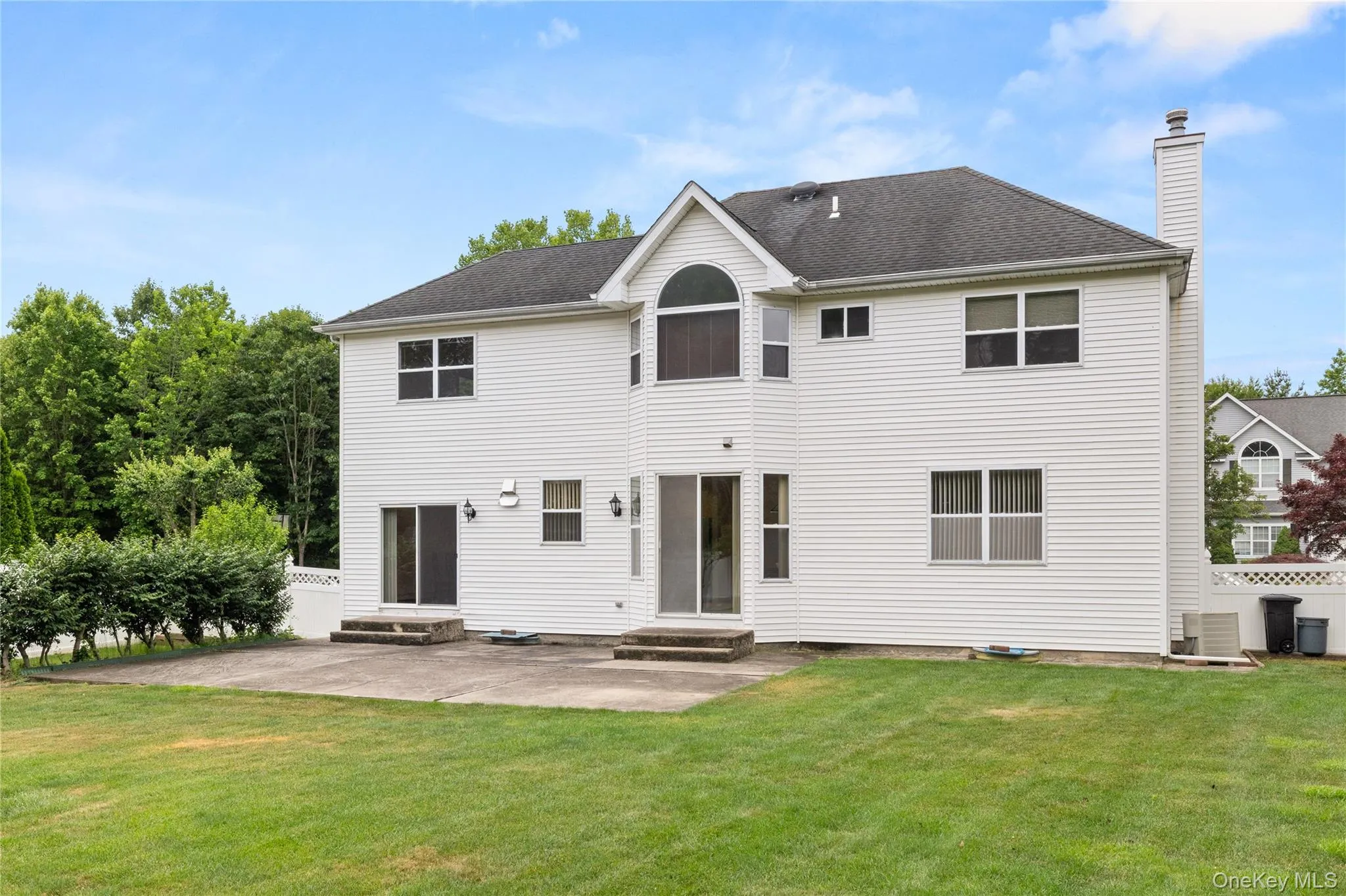 Rear exterior featuring white vinyl siding, a peaked roofline, and a prominent chimney Rear exterior featuring white vinyl siding, a peaked roofline, and a prominent chimney