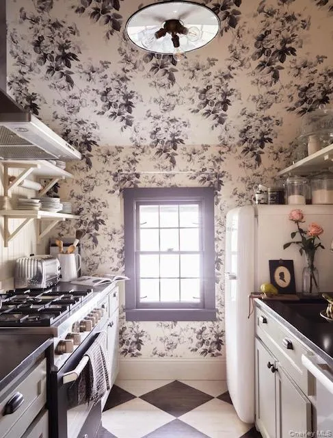 Kitchen featuring wallpapered walls, stainless steel gas range oven, white cabinets, dark countertops, and freestanding refrigerator Kitchen featuring wallpapered walls, stainless steel gas range oven, white cabinets, dark countertops, and freestanding refrigerator