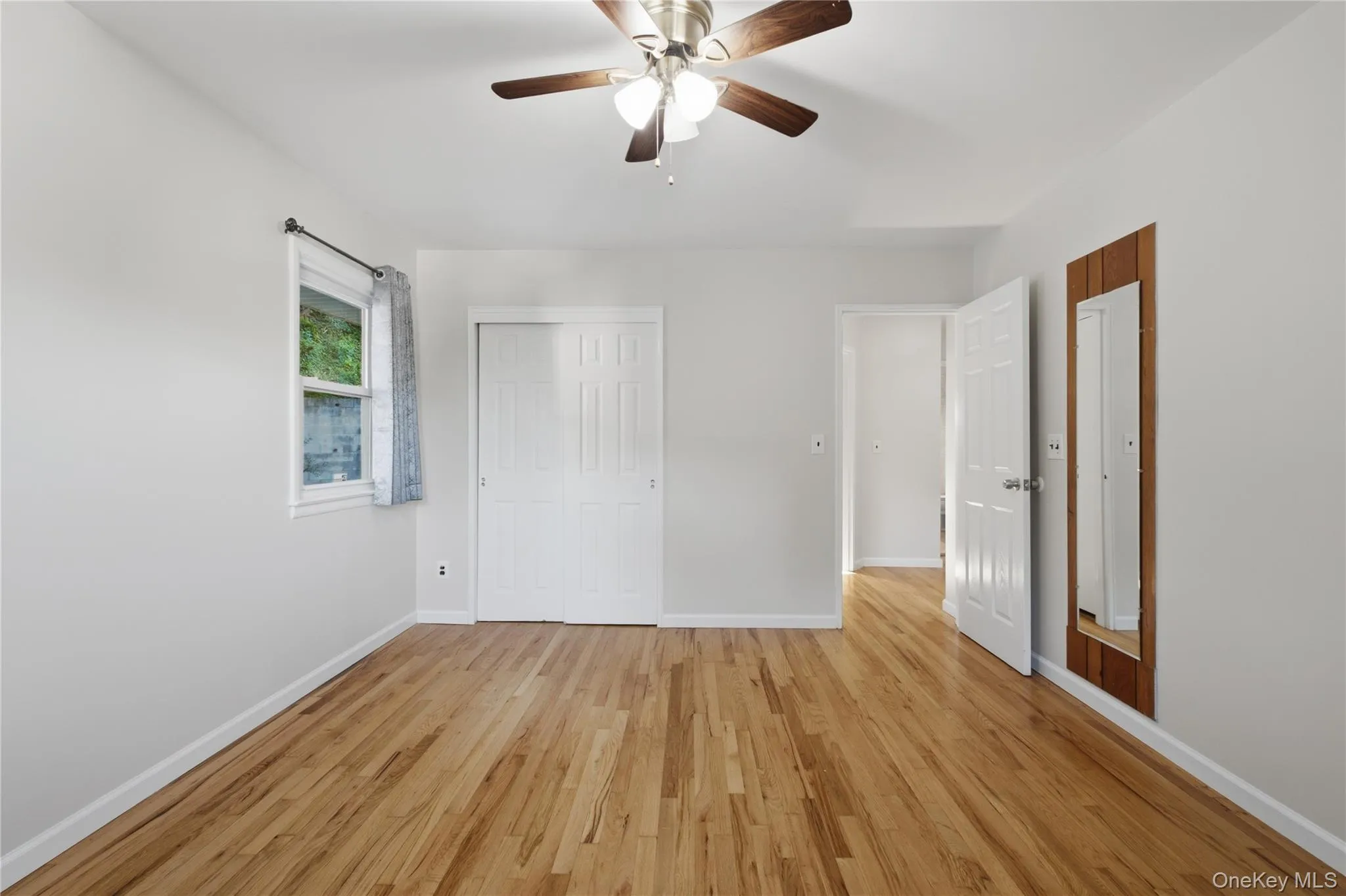 Bright room featuring wood-finish flooring, a ceiling fan with light fixture, and a window with natural light Bright room featuring wood-finish flooring, a ceiling fan with light fixture, and a window with natural light