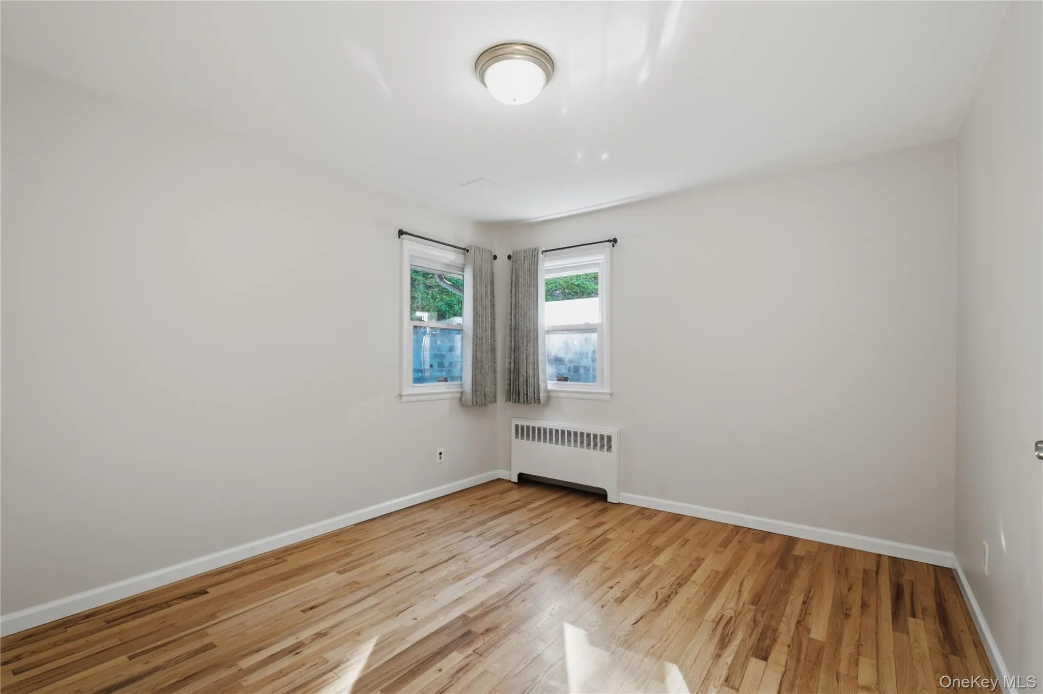 Room featuring wood-finish flooring, white baseboards, and neutral wall paint Room featuring wood-finish flooring, white baseboards, and neutral wall paint