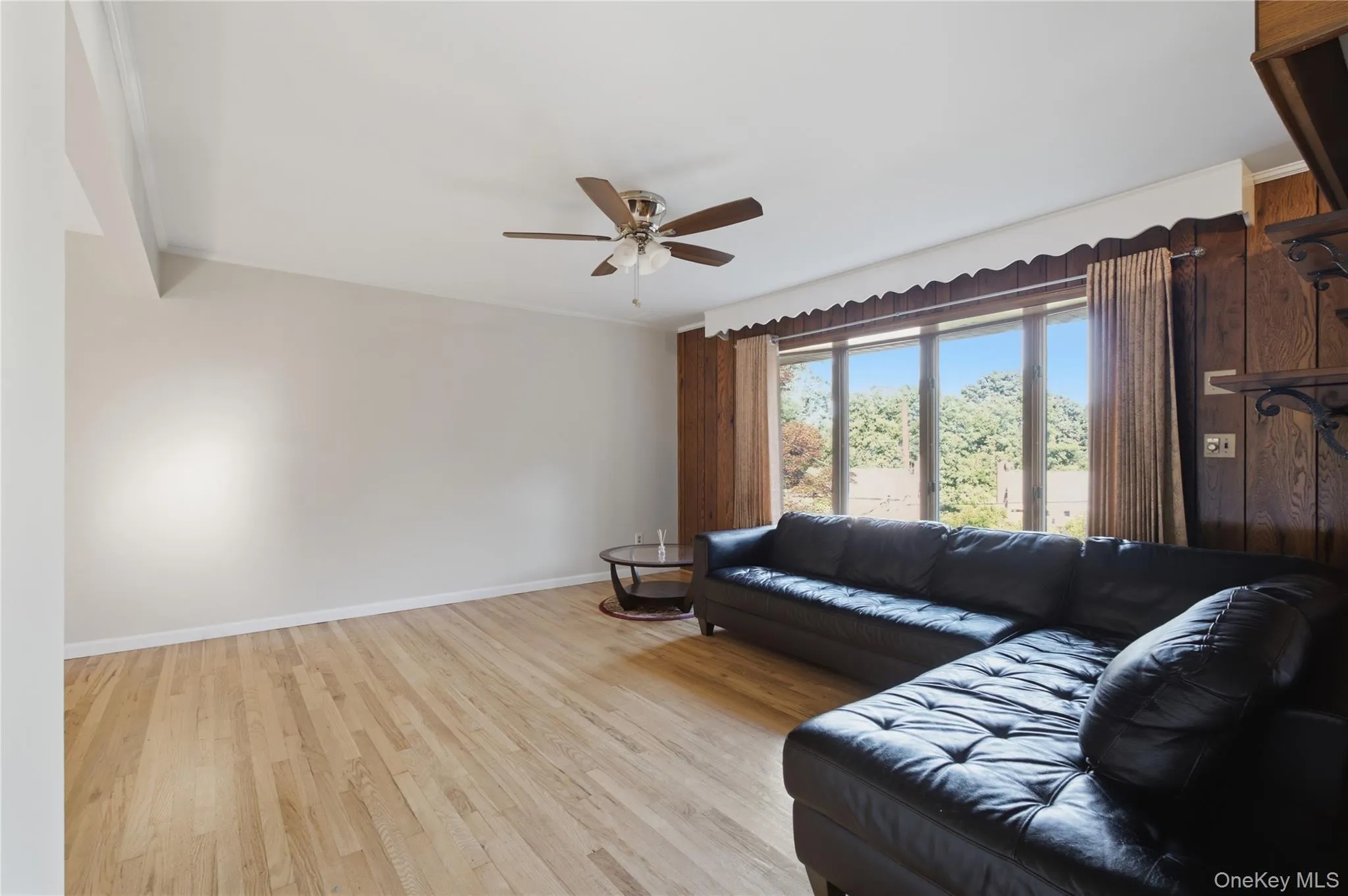 Spacious living area featuring light wood-finish flooring, a contemporary ceiling fan, and a large bay window Spacious living area featuring light wood-finish flooring, a contemporary ceiling fan, and a large bay window