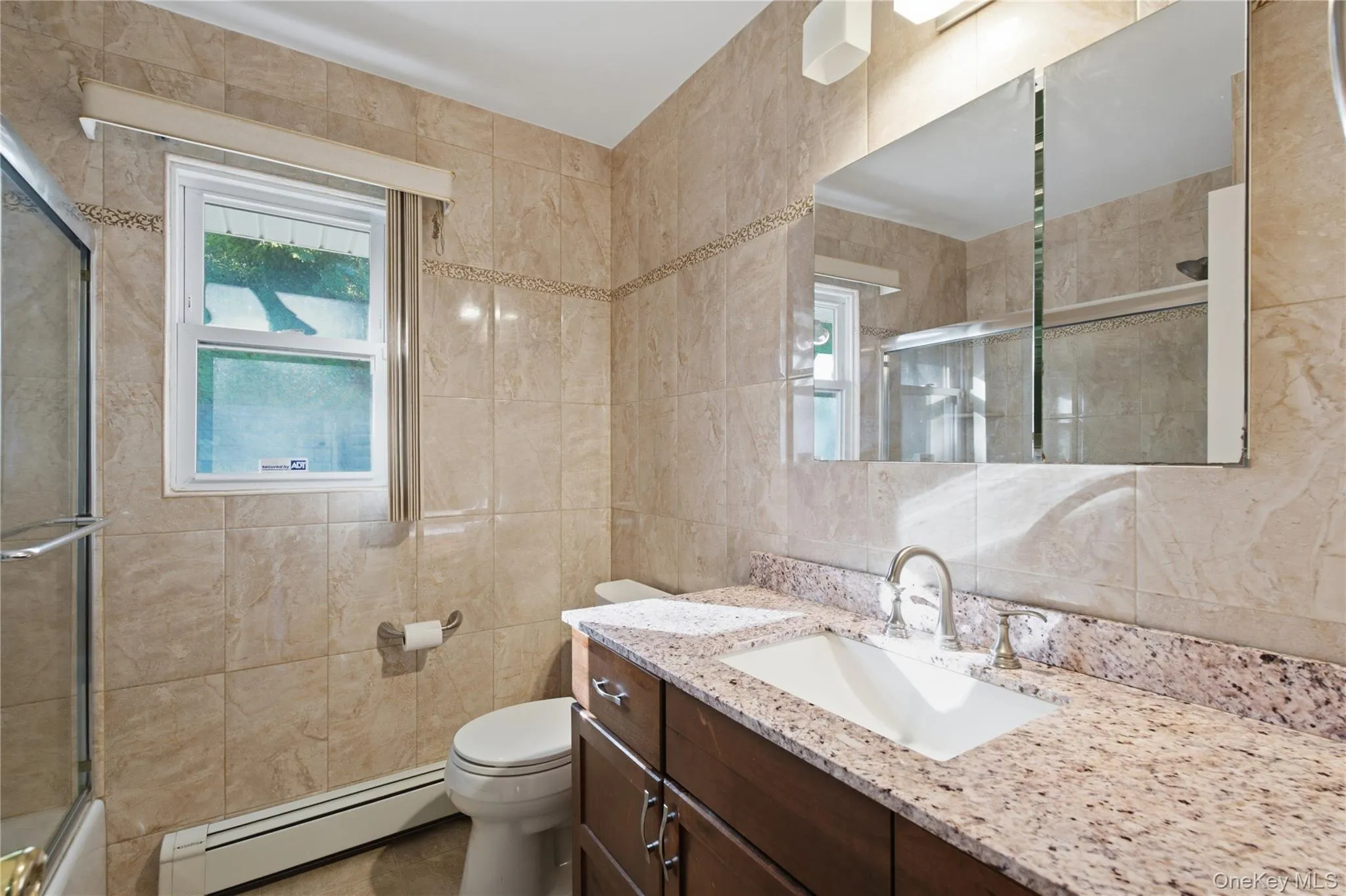 Bathroom featuring full-height tiled walls, a window with a valance, and a vanity with a stone-finish countertop and undermount sink Bathroom featuring full-height tiled walls, a window with a valance, and a vanity with a stone-finish countertop and undermount sink