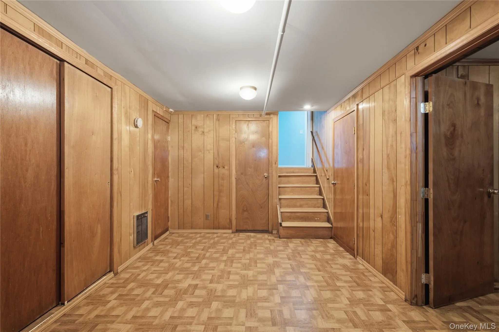 Finished basement room featuring extensive wood paneling, patterned wood-finish flooring, and multiple built-in storage closets Finished basement room featuring extensive wood paneling, patterned wood-finish flooring, and multiple built-in storage closets