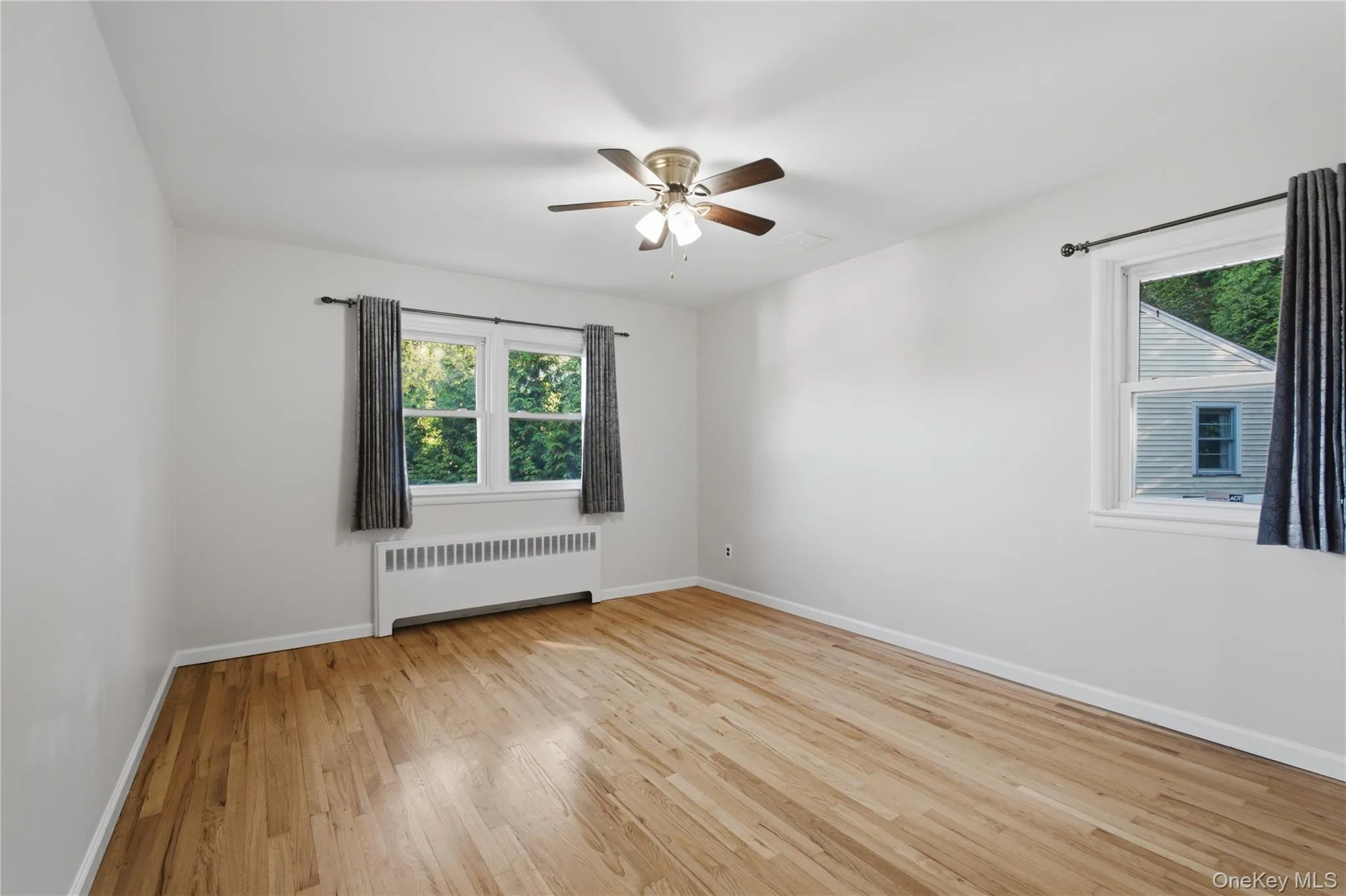 Spacious room featuring wood-finish flooring, white walls, and a ceiling fan Spacious room featuring wood-finish flooring, white walls, and a ceiling fan