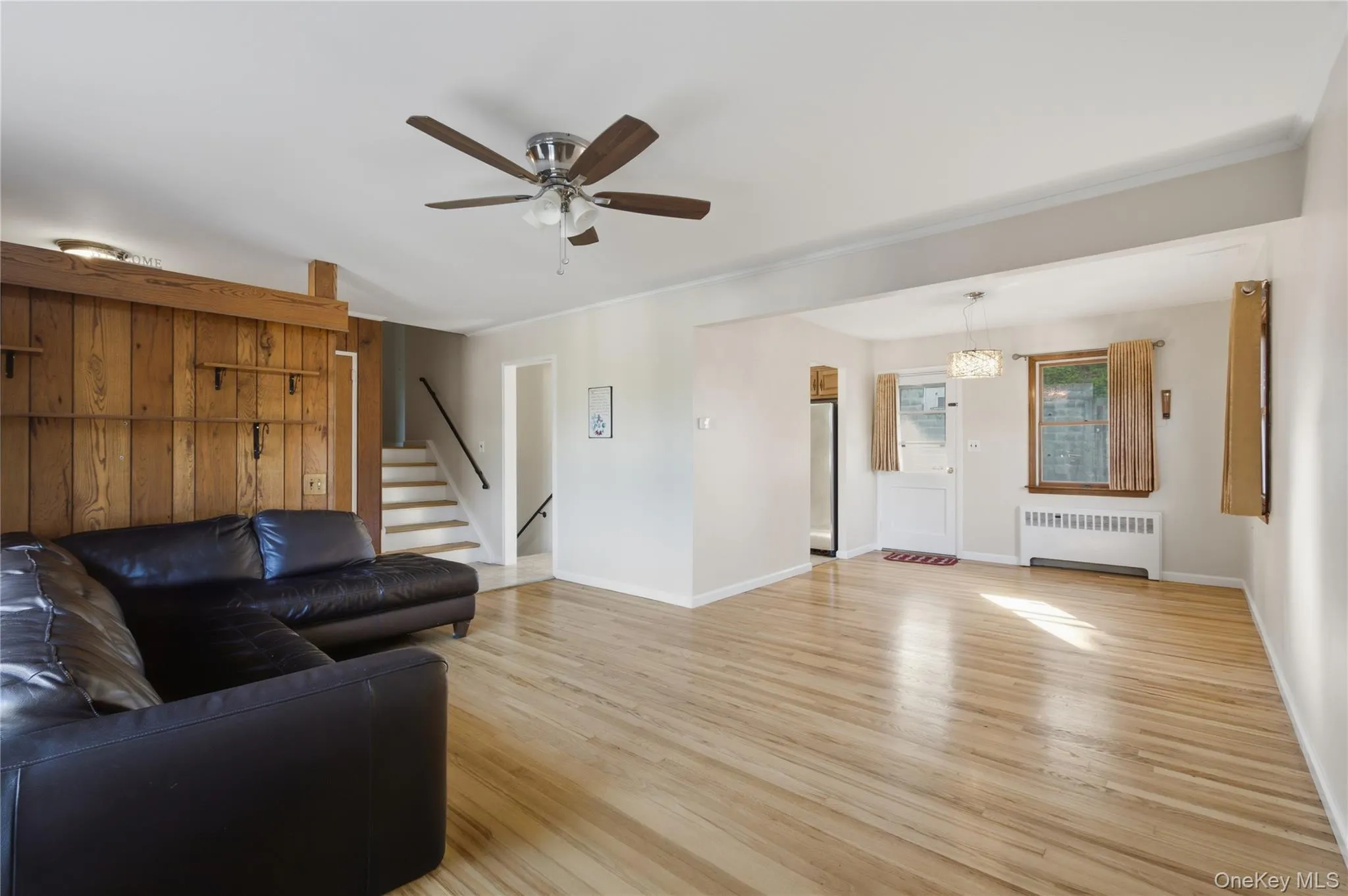 Bright interior featuring wood-finish flooring, a wood paneled accent wall, and a ceiling fan Bright interior featuring wood-finish flooring, a wood paneled accent wall, and a ceiling fan