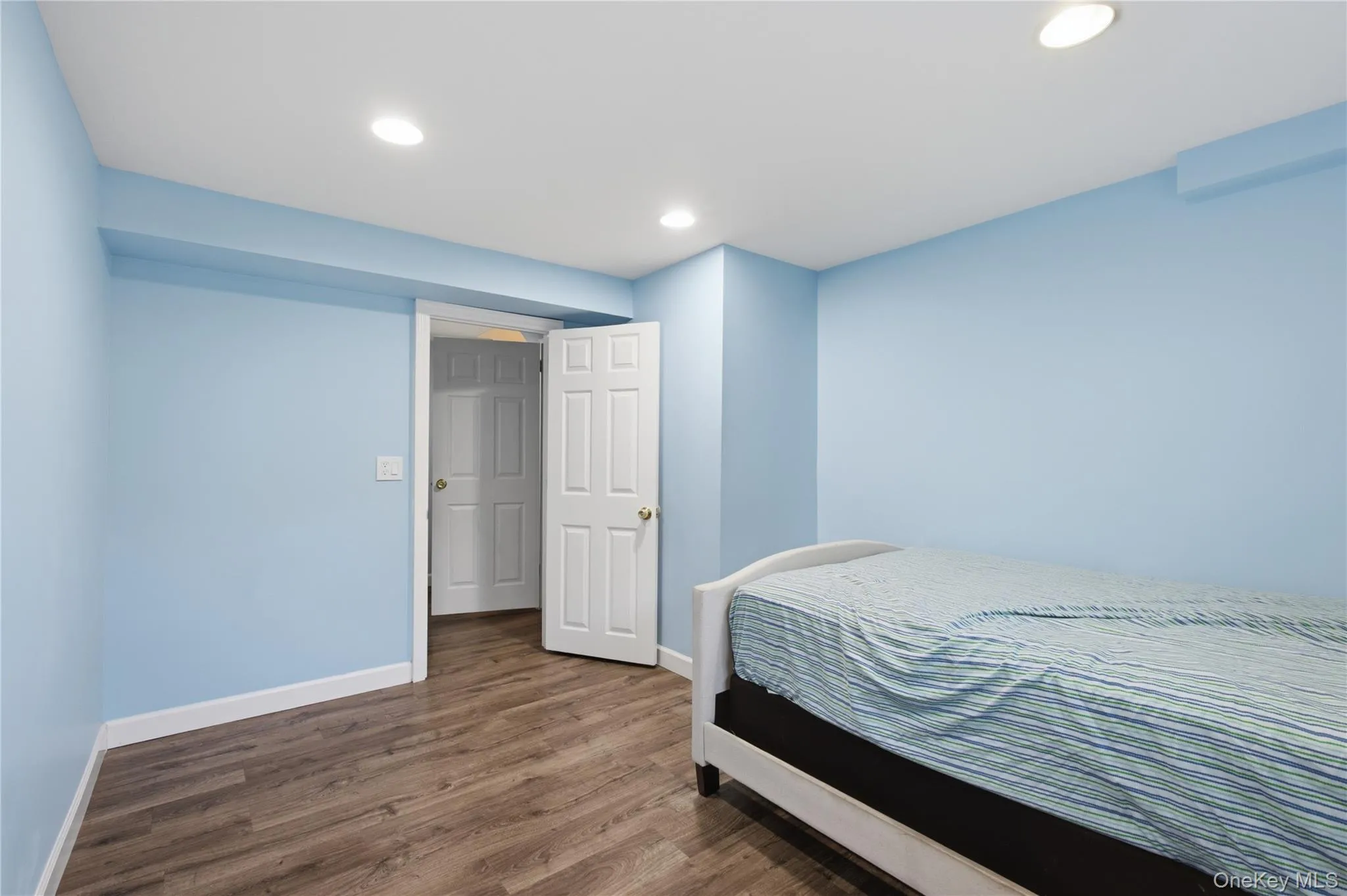 Interior room featuring wood-finish flooring, recessed ceiling lighting, and a white six-panel door Interior room featuring wood-finish flooring, recessed ceiling lighting, and a white six-panel door
