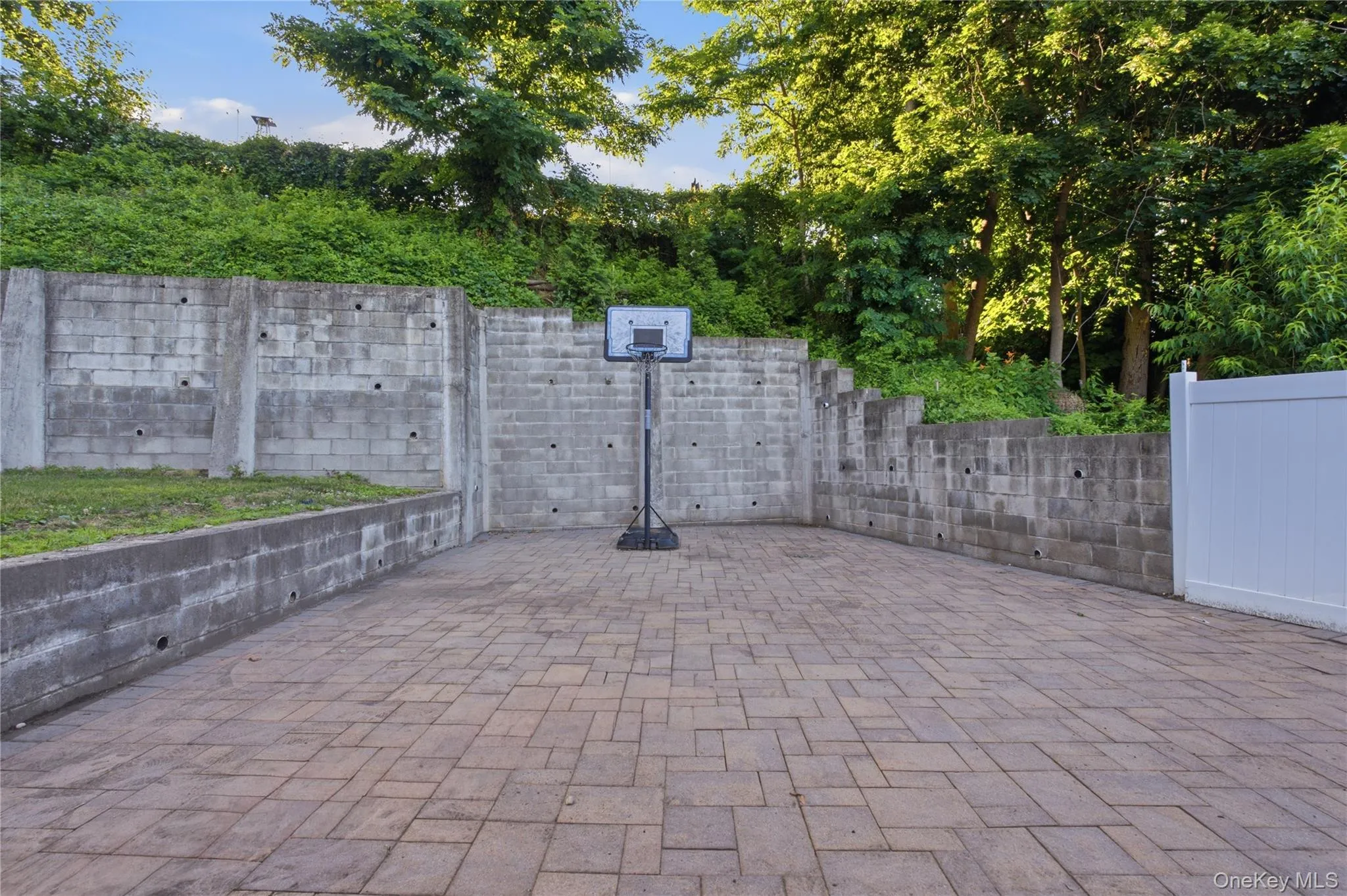 Spacious paver patio area with concrete retaining walls and mature foliage Spacious paver patio area with concrete retaining walls and mature foliage