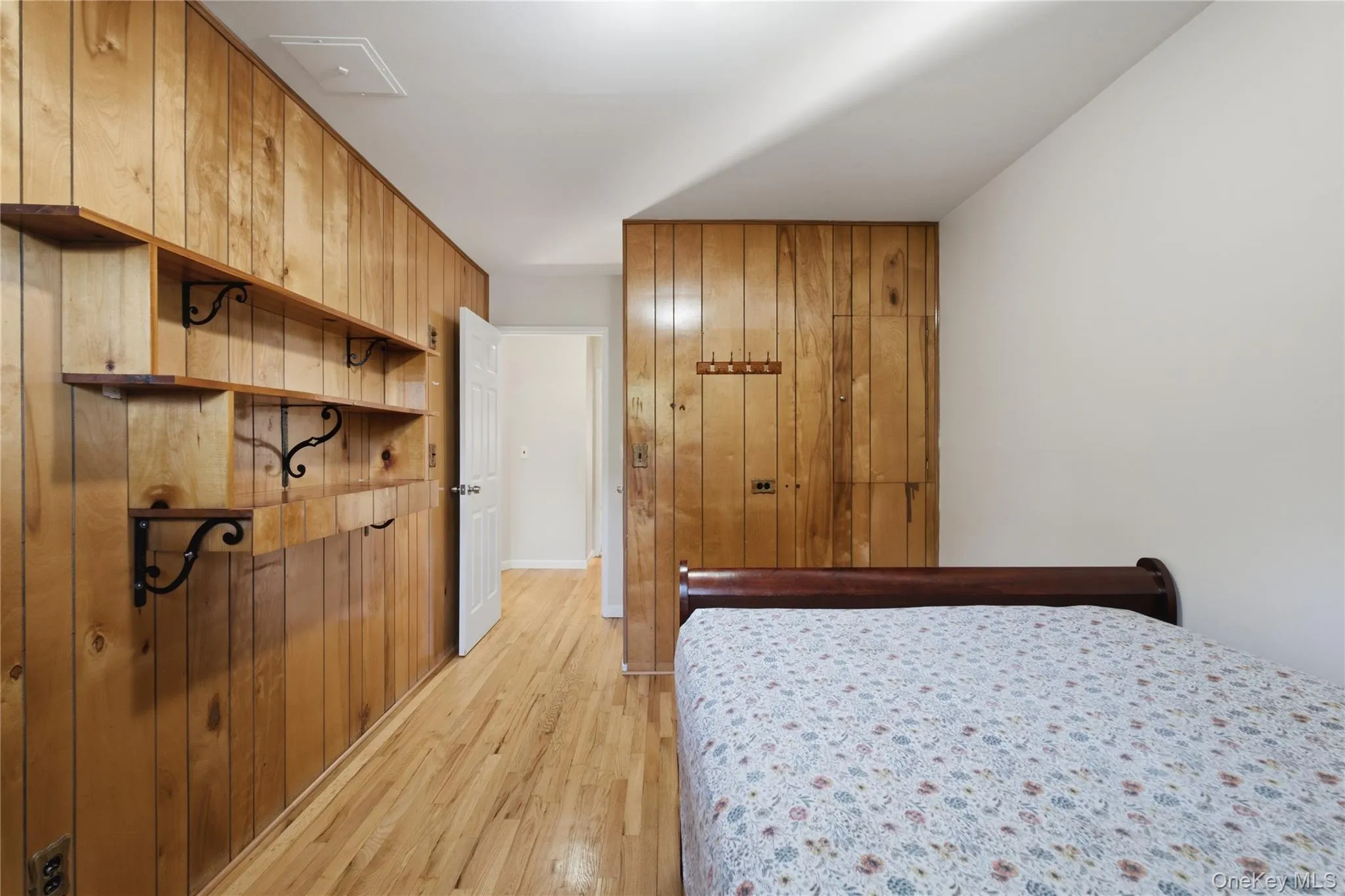 Wood-paneled wall with built-in shelving, wood-finish flooring, white door, and white ceiling Wood-paneled wall with built-in shelving, wood-finish flooring, white door, and white ceiling