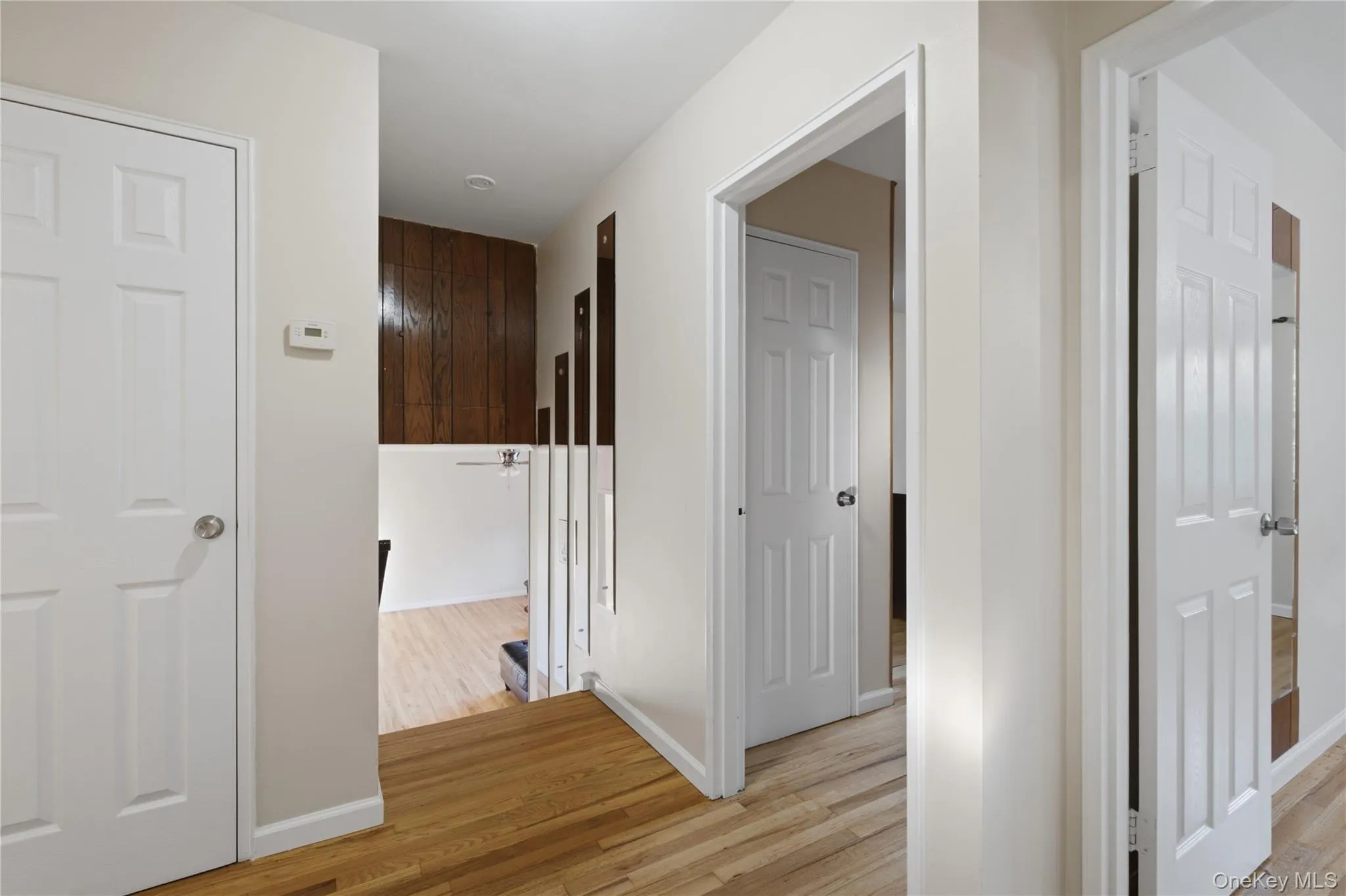 Hallway featuring wood-finish flooring, white paneled doors, and light-toned walls Hallway featuring wood-finish flooring, white paneled doors, and light-toned walls