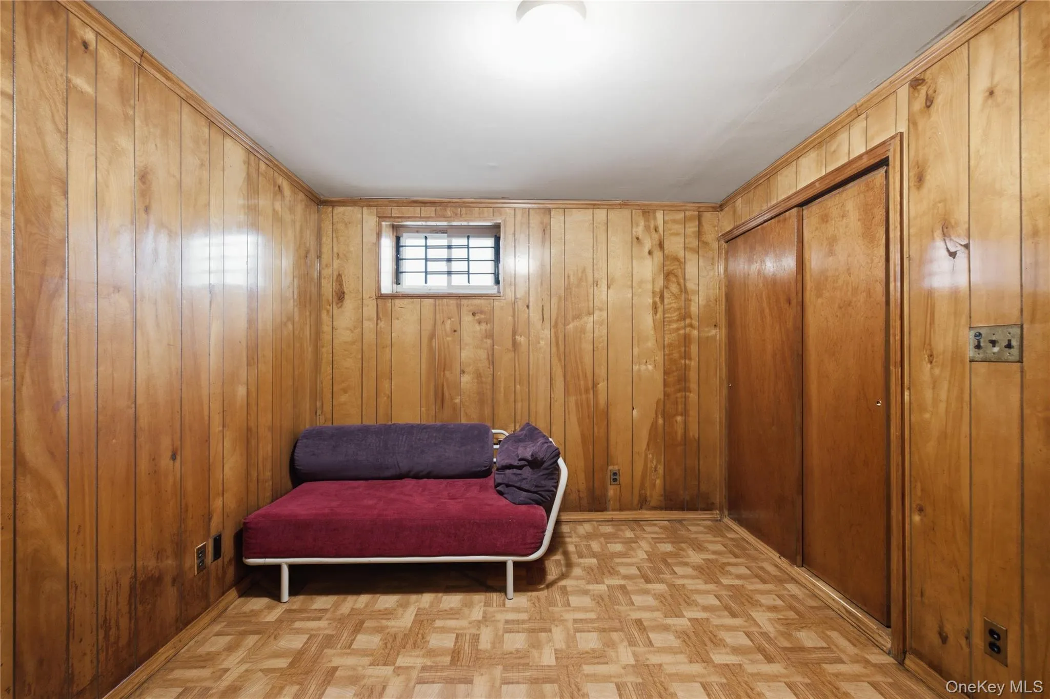 Room featuring vertical wood paneling, a patterned wood-finish floor, and a built-in closet with sliding wood doors Room featuring vertical wood paneling, a patterned wood-finish floor, and a built-in closet with sliding wood doors