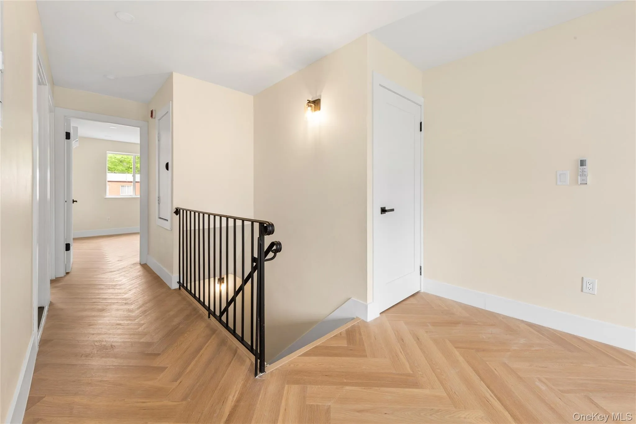 Hallway featuring herringbone wood-finish flooring, a contemporary black metal railing, and a wall-mounted sconce Hallway featuring herringbone wood-finish flooring, a contemporary black metal railing, and a wall-mounted sconce