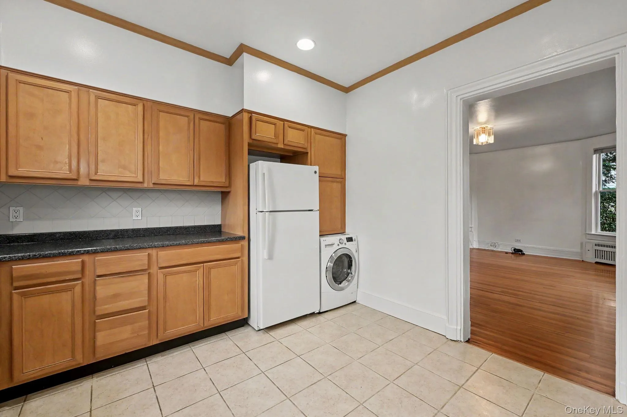 Kitchen featuring light wood cabinetry, dark countertops, a backsplash, and tile flooring Kitchen featuring light wood cabinetry, dark countertops, a backsplash, and tile flooring