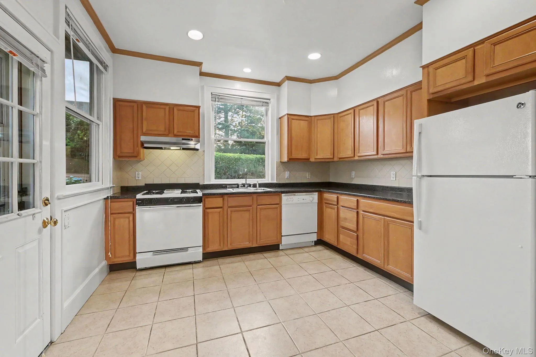 Kitchen featuring wood cabinetry, dark countertops, a refrigerator, a range, and a dishwasher Kitchen featuring wood cabinetry, dark countertops, a refrigerator, a range, and a dishwasher