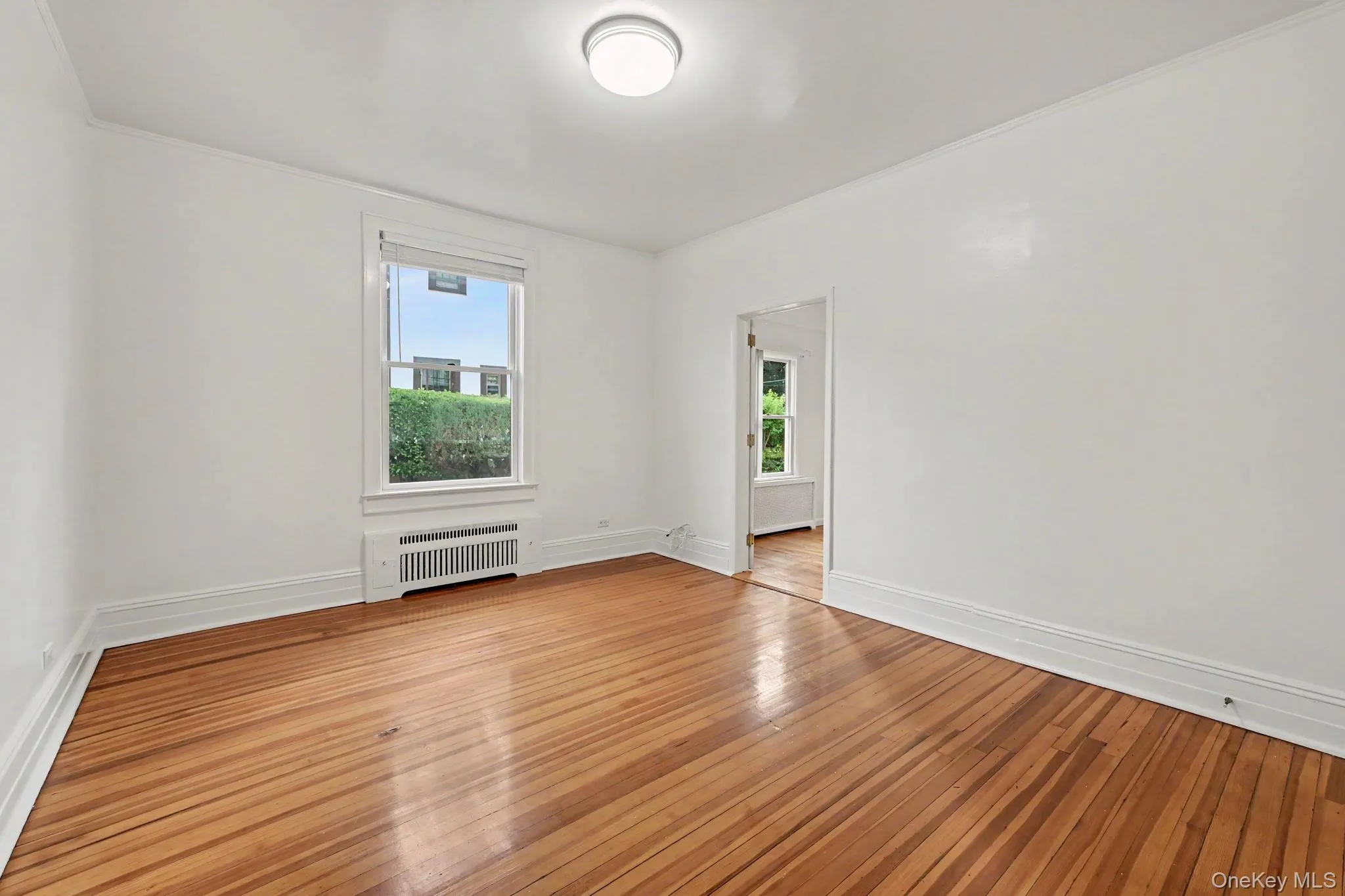 Hardwood flooring throughout, featuring a white trim package, single window, and flush-mount ceiling light Hardwood flooring throughout, featuring a white trim package, single window, and flush-mount ceiling light