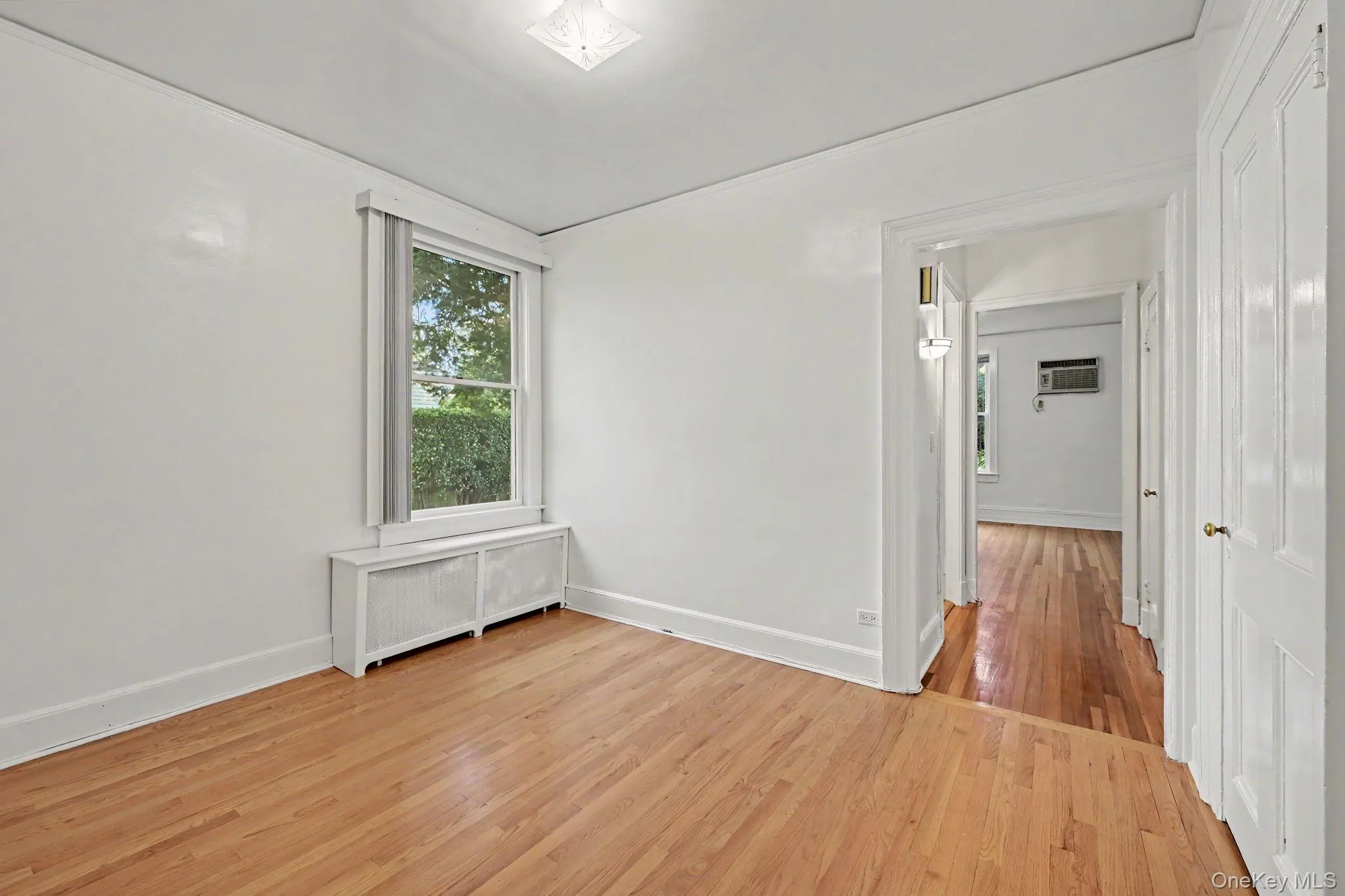 Bedroom featuring wood-finish flooring, white painted walls, and a window with an integrated radiator cover Bedroom featuring wood-finish flooring, white painted walls, and a window with an integrated radiator cover