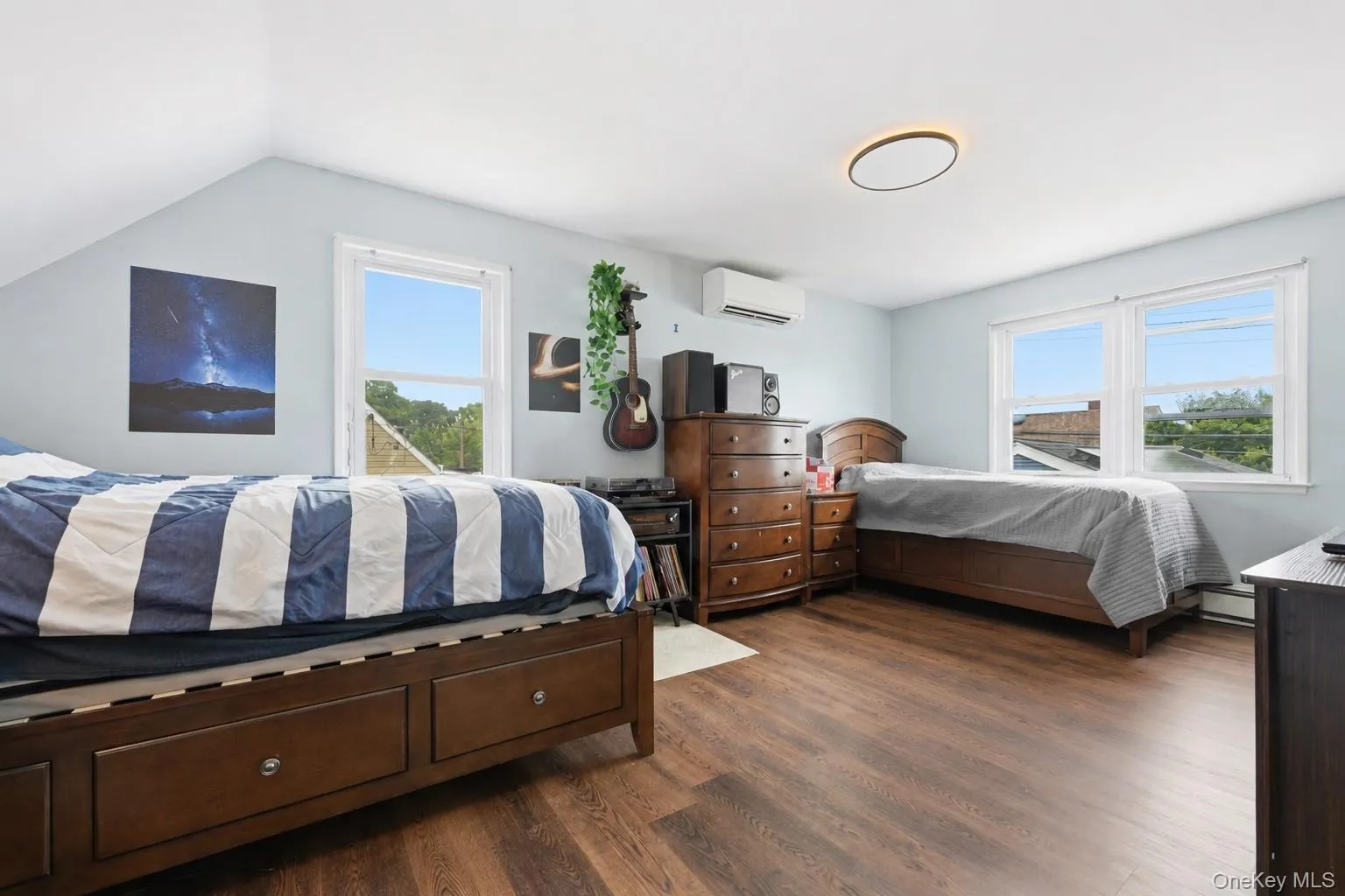 Bedroom featuring wood-finish flooring, light blue wall paint, and white trim windows Bedroom featuring wood-finish flooring, light blue wall paint, and white trim windows