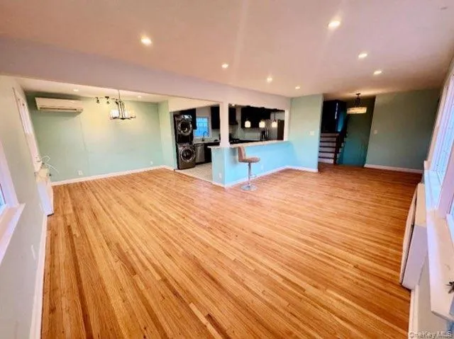 Unfurnished living room with an AC wall unit, a notable chandelier, and light hardwood / wood-style floors Unfurnished living room with an AC wall unit, a notable chandelier, and light hardwood / wood-style floors