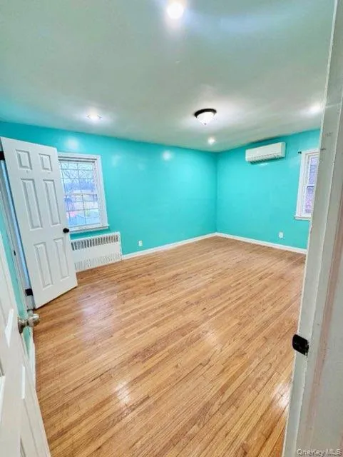 Unfurnished room featuring light hardwood / wood-style flooring, radiator heating unit, and a wall unit AC Unfurnished room featuring light hardwood / wood-style flooring, radiator heating unit, and a wall unit AC
