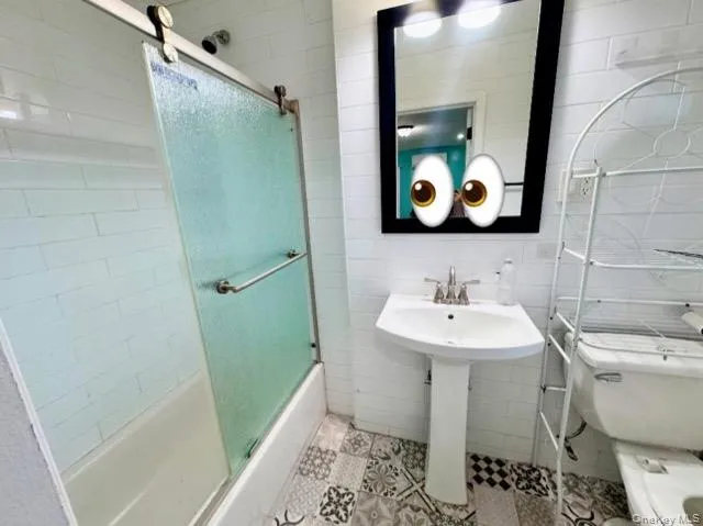 Bathroom with toilet, combined bath / shower with glass door, and tile walls Bathroom with toilet, combined bath / shower with glass door, and tile walls