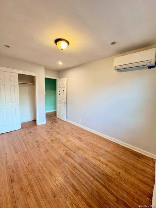 Unfurnished bedroom with hardwood / wood-style floors, a wall unit AC, and a closet Unfurnished bedroom with hardwood / wood-style floors, a wall unit AC, and a closet