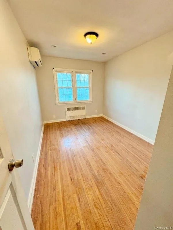 Spare room featuring radiator, a wall mounted air conditioner, and light wood-type flooring Spare room featuring radiator, a wall mounted air conditioner, and light wood-type flooring