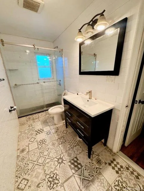 Bathroom featuring vanity, a shower with shower door, tile walls, and toilet Bathroom featuring vanity, a shower with shower door, tile walls, and toilet