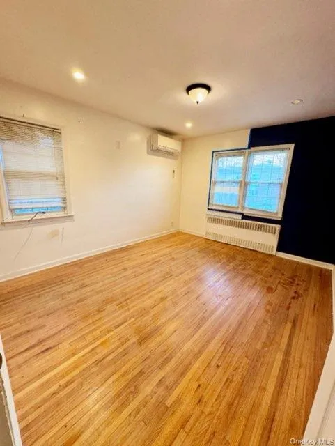 Spare room with radiator heating unit, light hardwood / wood-style floors, and an AC wall unit Spare room with radiator heating unit, light hardwood / wood-style floors, and an AC wall unit