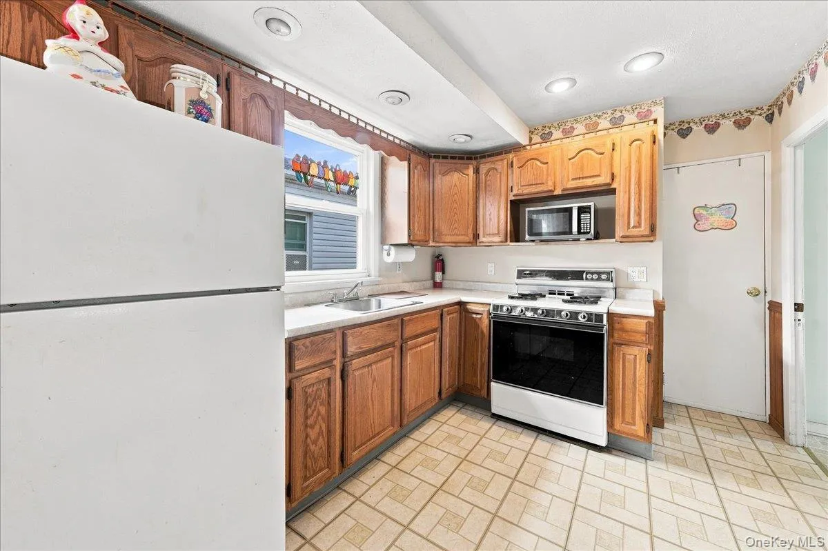 Wood-finish cabinetry, recessed lighting, and a window above the sink Wood-finish cabinetry, recessed lighting, and a window above the sink