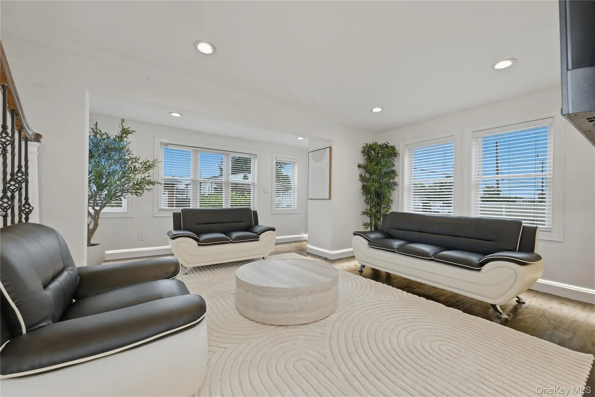 Bright interior space featuring recessed lighting, multiple windows with blinds, wood-finish flooring, and a decorative wrought iron staircase railing Bright interior space featuring recessed lighting, multiple windows with blinds, wood-finish flooring, and a decorative wrought iron staircase railing