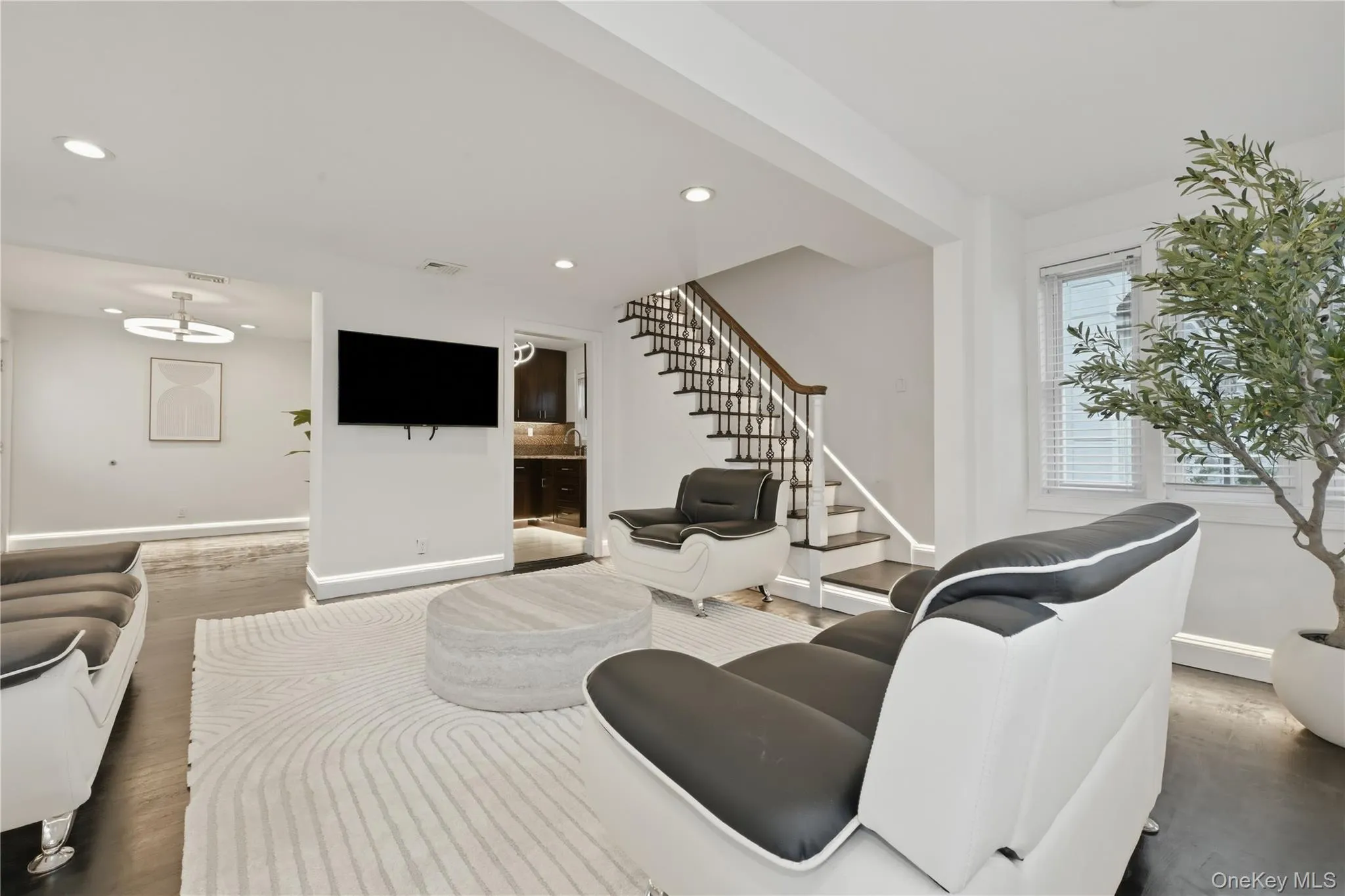 Living area featuring dark wood-finish flooring and a contemporary staircase with white risers and dark wood handrails Living area featuring dark wood-finish flooring and a contemporary staircase with white risers and dark wood handrails