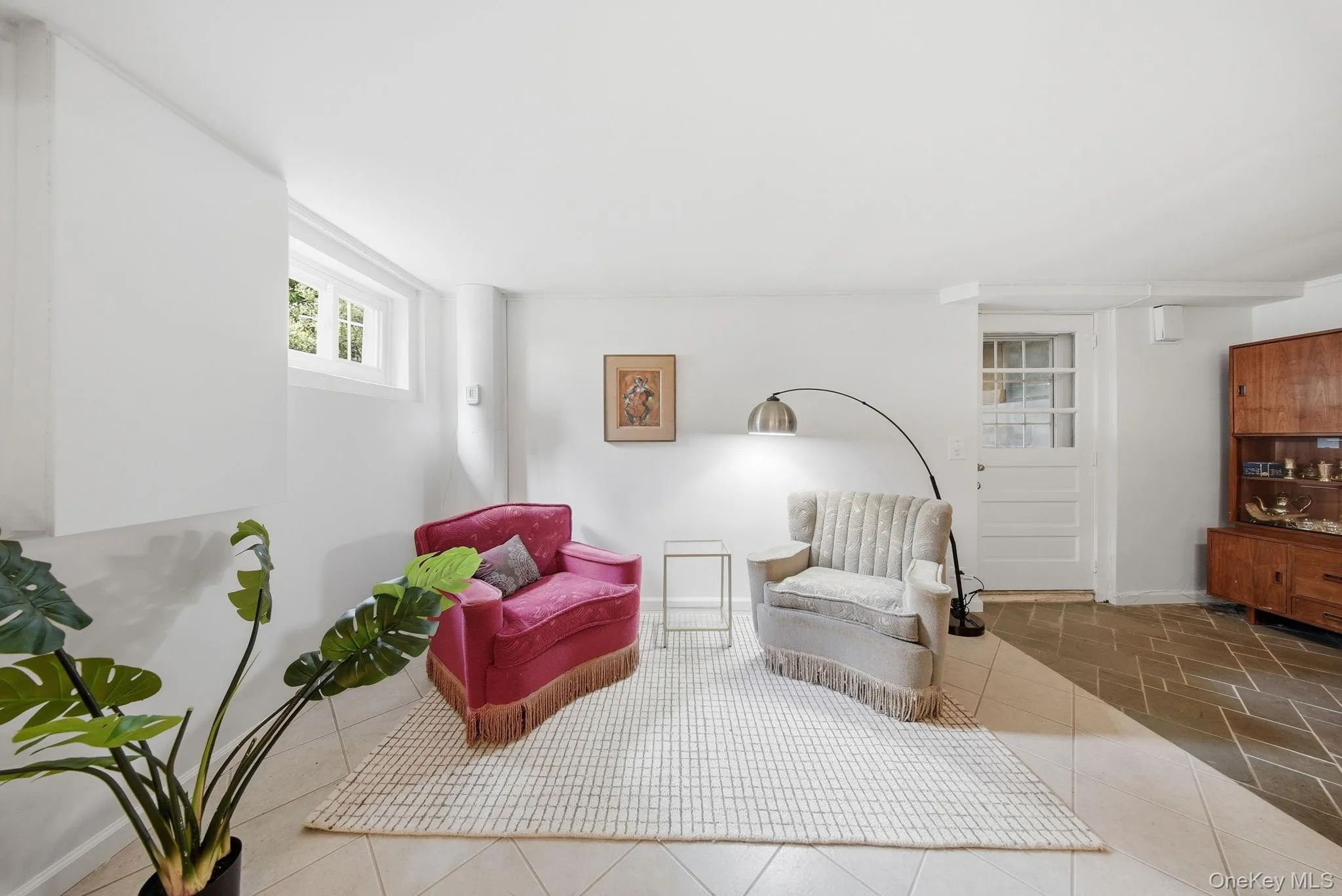 Bright living area featuring a white window, light-colored square tile flooring, and a paneled door with glass inserts Bright living area featuring a white window, light-colored square tile flooring, and a paneled door with glass inserts