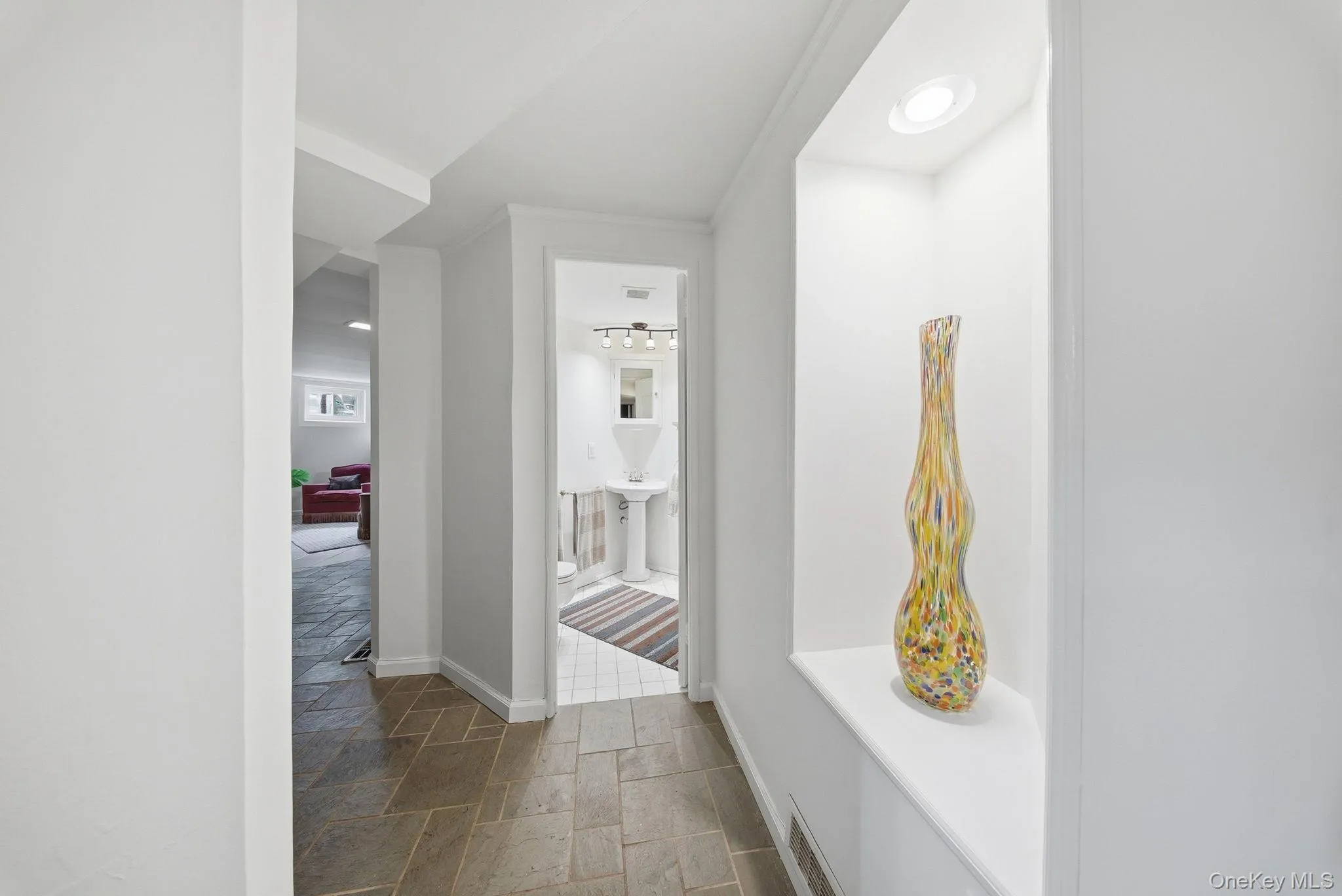 Hallway featuring stone tile flooring, a recessed wall niche with integrated lighting, and white baseboard trim Hallway featuring stone tile flooring, a recessed wall niche with integrated lighting, and white baseboard trim