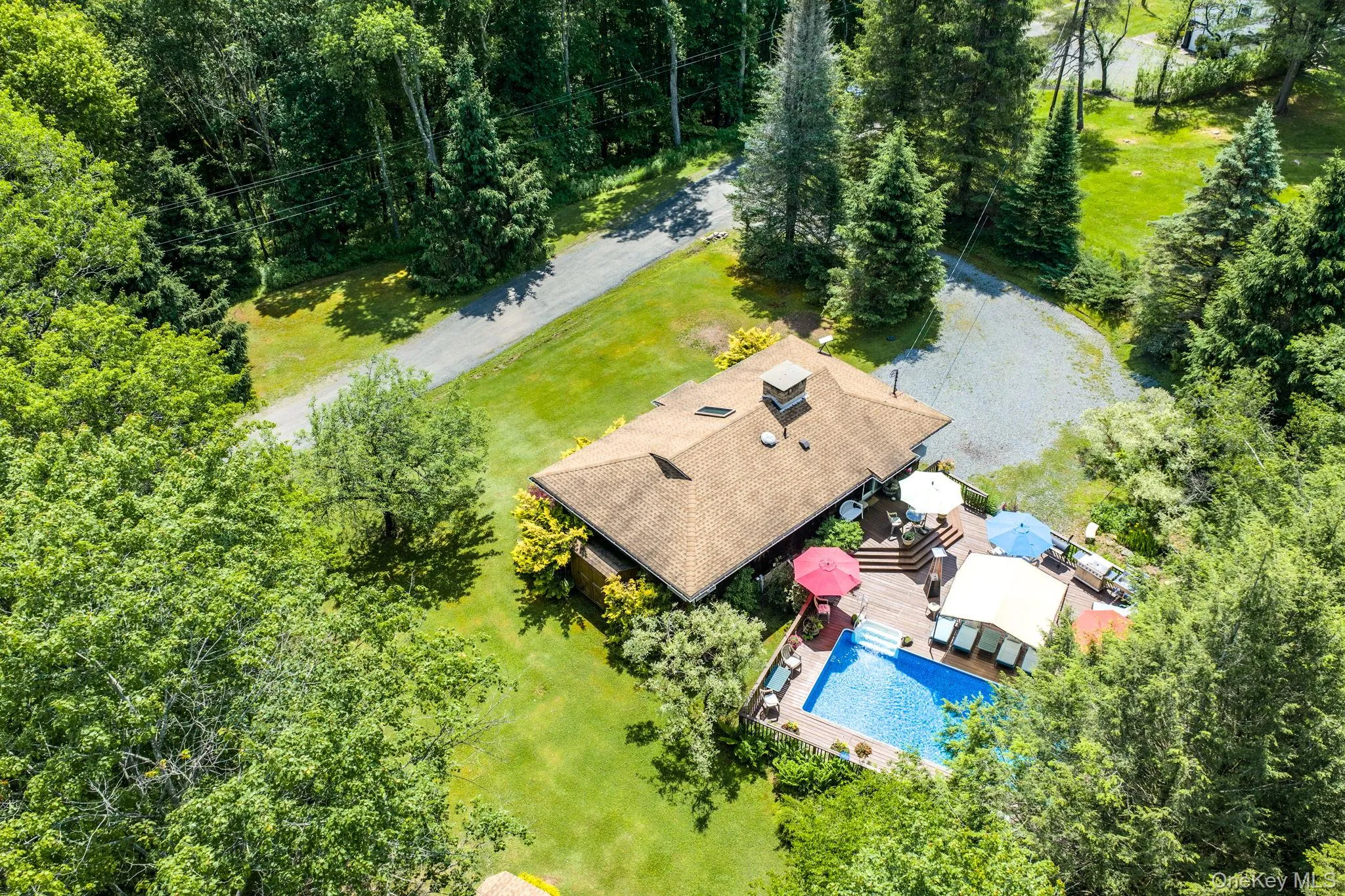 Expansive property featuring a private swimming pool, surrounding wood deck, and a gravel driveway Expansive property featuring a private swimming pool, surrounding wood deck, and a gravel driveway