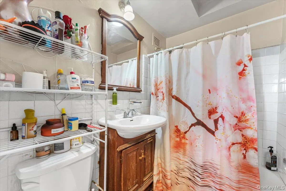 Full bath featuring backsplash, vanity, toilet, curtained shower, and tile walls Full bath featuring backsplash, vanity, toilet, curtained shower, and tile walls