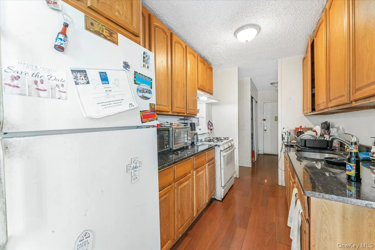 Kitchen with white appliances, a sink, wood finished floors, under cabinet range hood, and a textured ceiling Kitchen with white appliances, a sink, wood finished floors, under cabinet range hood, and a textured ceiling