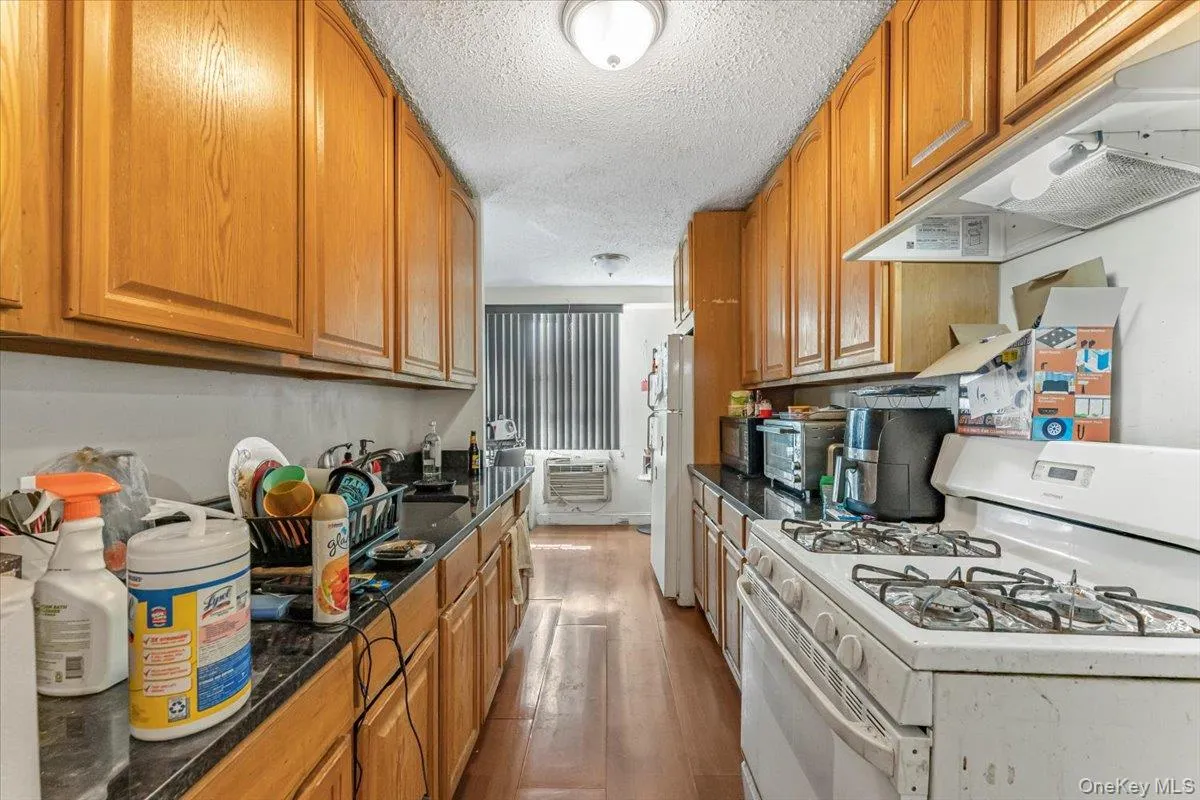 Kitchen with white appliances, under cabinet range hood, a textured ceiling, wood finished floors, and a sink Kitchen with white appliances, under cabinet range hood, a textured ceiling, wood finished floors, and a sink
