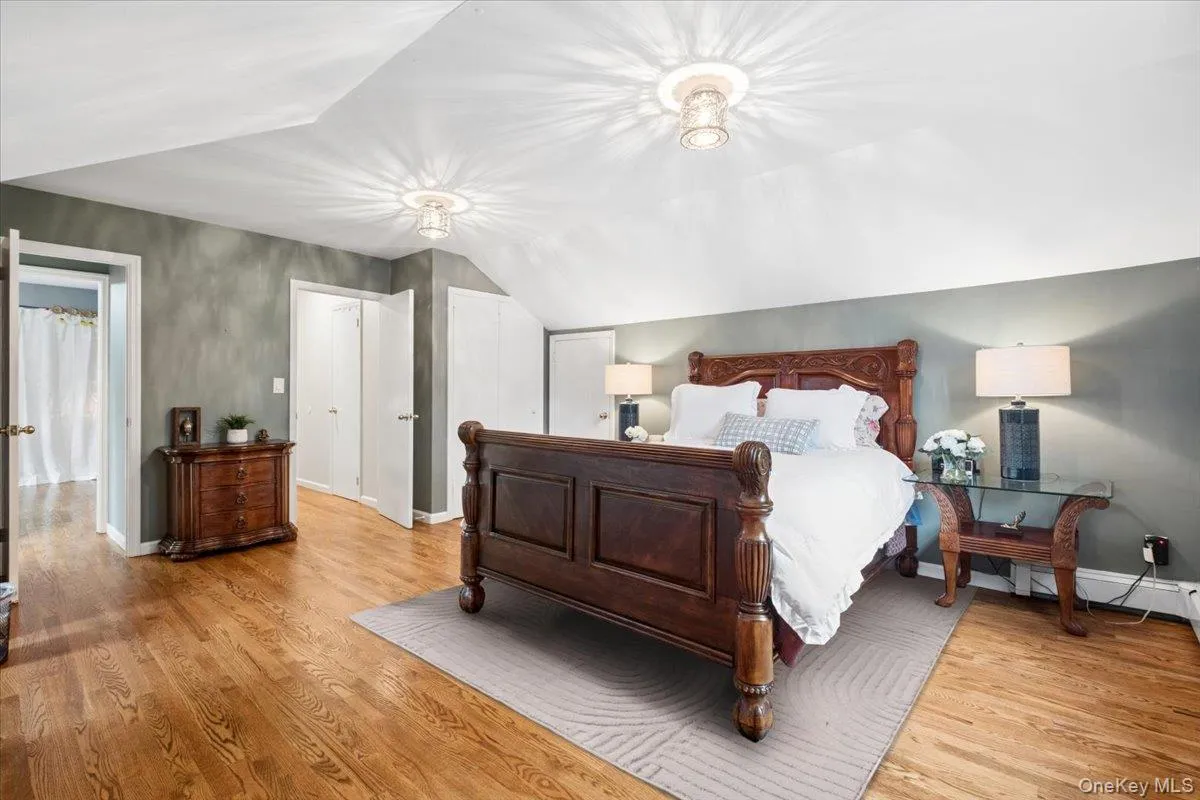 Hardwood flooring extends throughout this primary bedroom, featuring an angled ceiling and two walk-in-closets. Hardwood flooring extends throughout this primary bedroom, featuring an angled ceiling and two walk-in-closets.