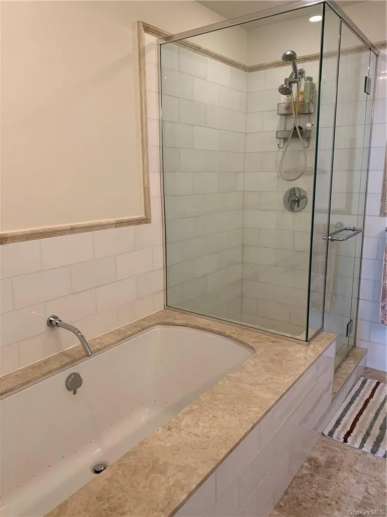 Bathroom featuring plus walk in shower, jacuzzi, tile patterned flooring, and tile walls Bathroom featuring plus walk in shower, jacuzzi, tile patterned flooring, and tile walls