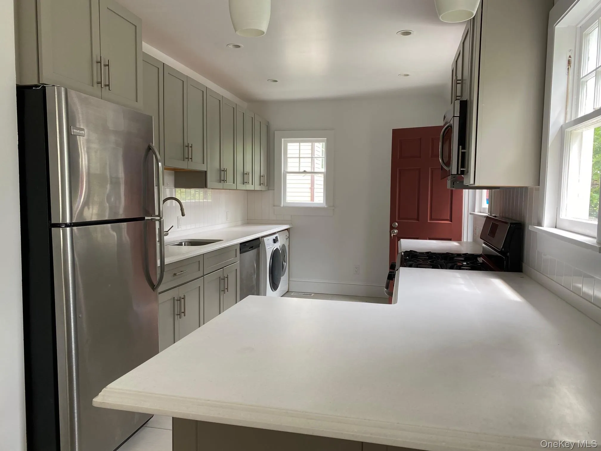 Contemporary kitchen featuring light gray cabinetry, stainless steel appliances, a white subway tile backsplash, and light-toned countertops Contemporary kitchen featuring light gray cabinetry, stainless steel appliances, a white subway tile backsplash, and light-toned countertops