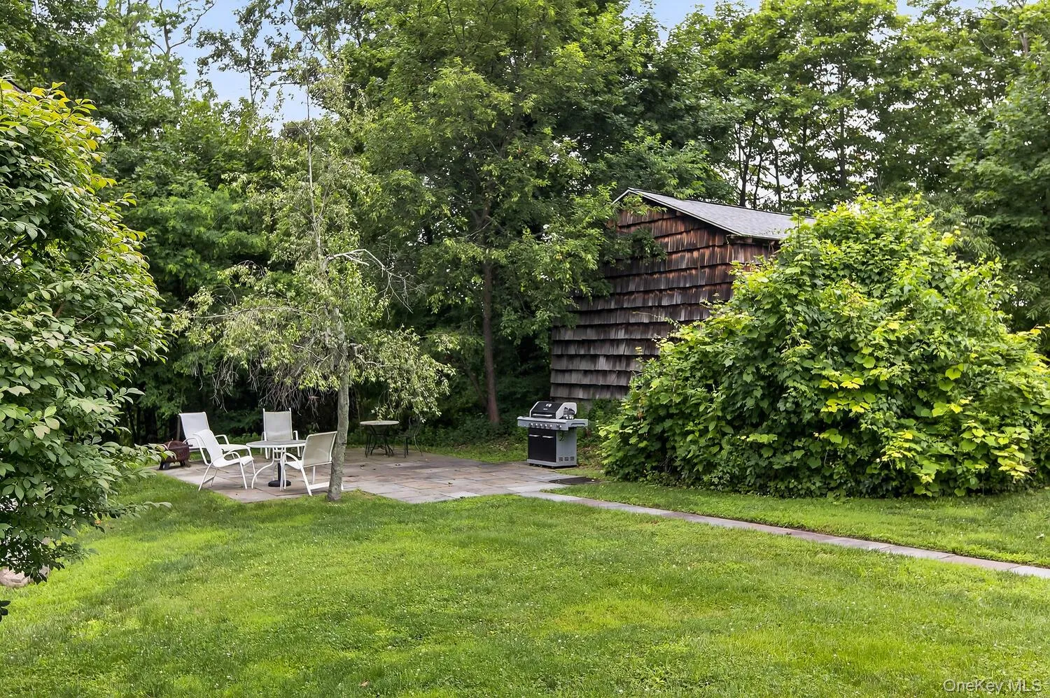 Expansive backyard featuring a common area with stone patio, mature trees, and barbeque Expansive backyard featuring a common area with stone patio, mature trees, and barbeque