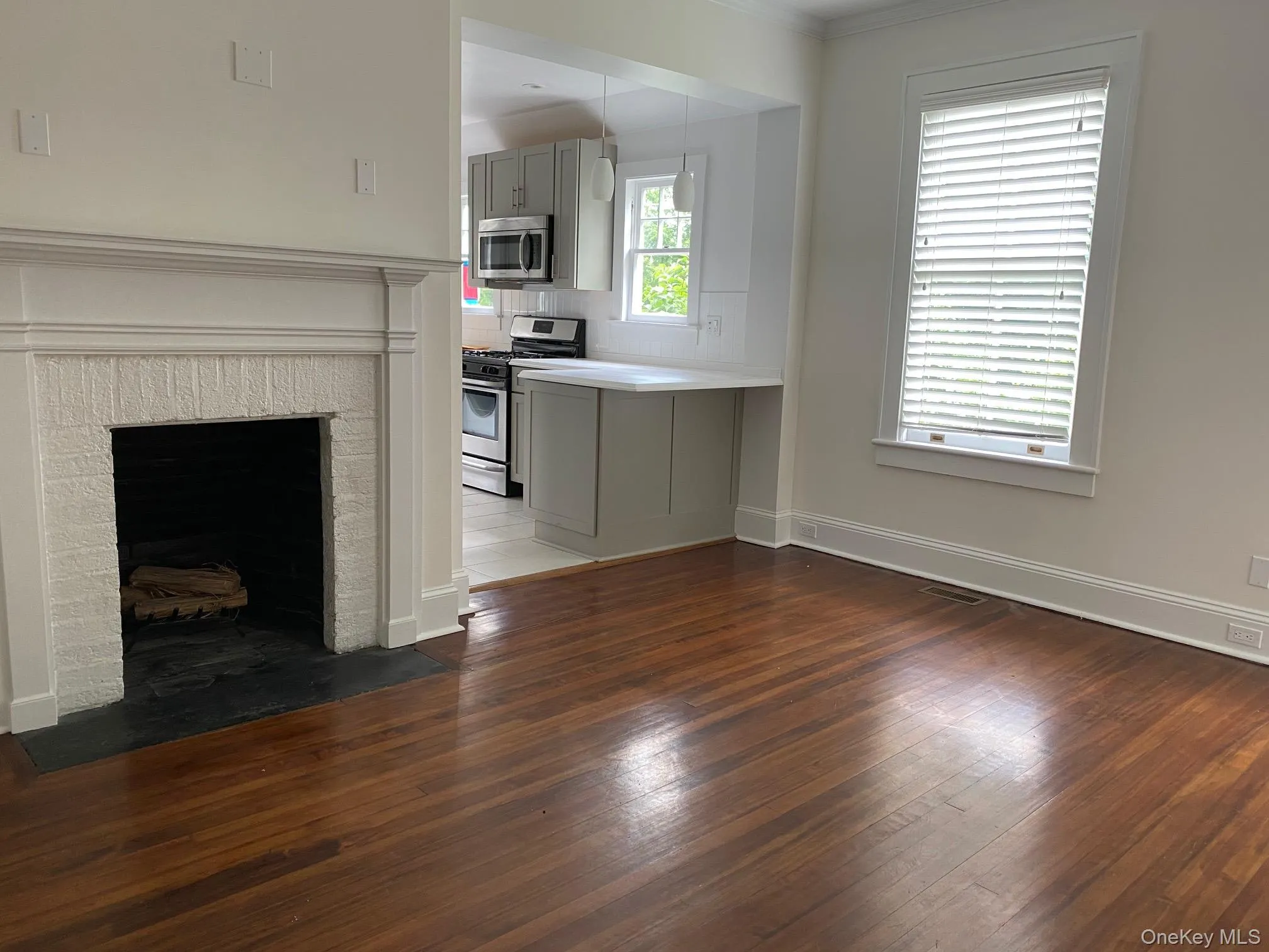 Living area featuring wood-finish flooring, a painted brick fireplace with a stone hearth, and a window with blinds Living area featuring wood-finish flooring, a painted brick fireplace with a stone hearth, and a window with blinds