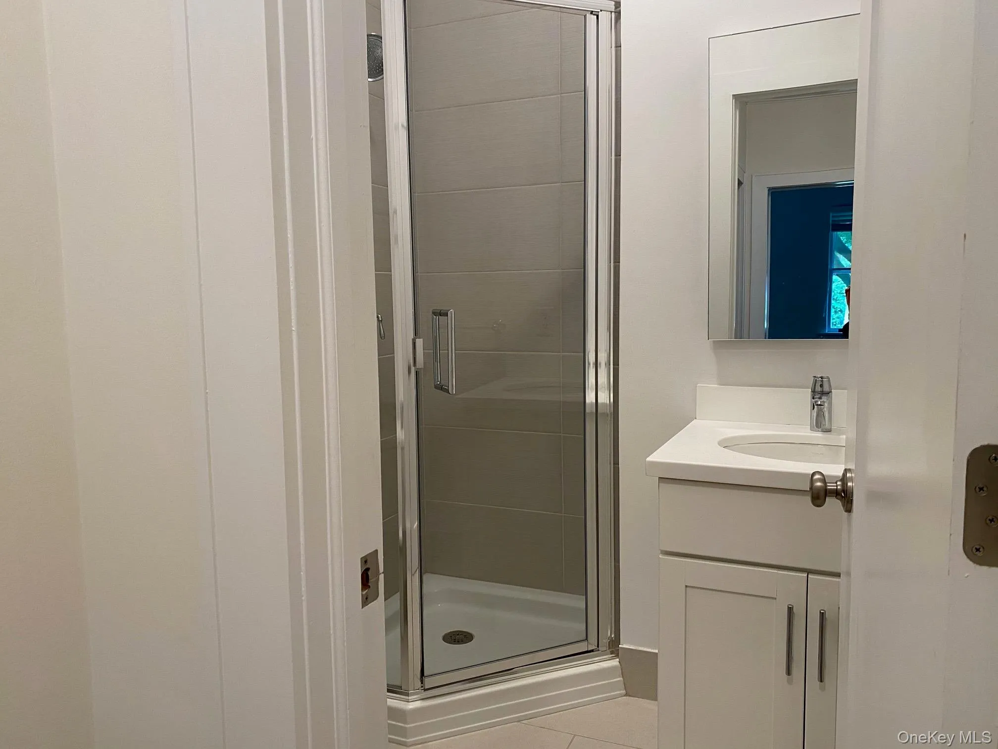 Contemporary bathroom featuring a glass-enclosed shower with horizontal tile surround, a single vanity with a white countertop and integrated sink, a framed mirror, and chrome fixtures Contemporary bathroom featuring a glass-enclosed shower with horizontal tile surround, a single vanity with a white countertop and integrated sink, a framed mirror, and chrome fixtures