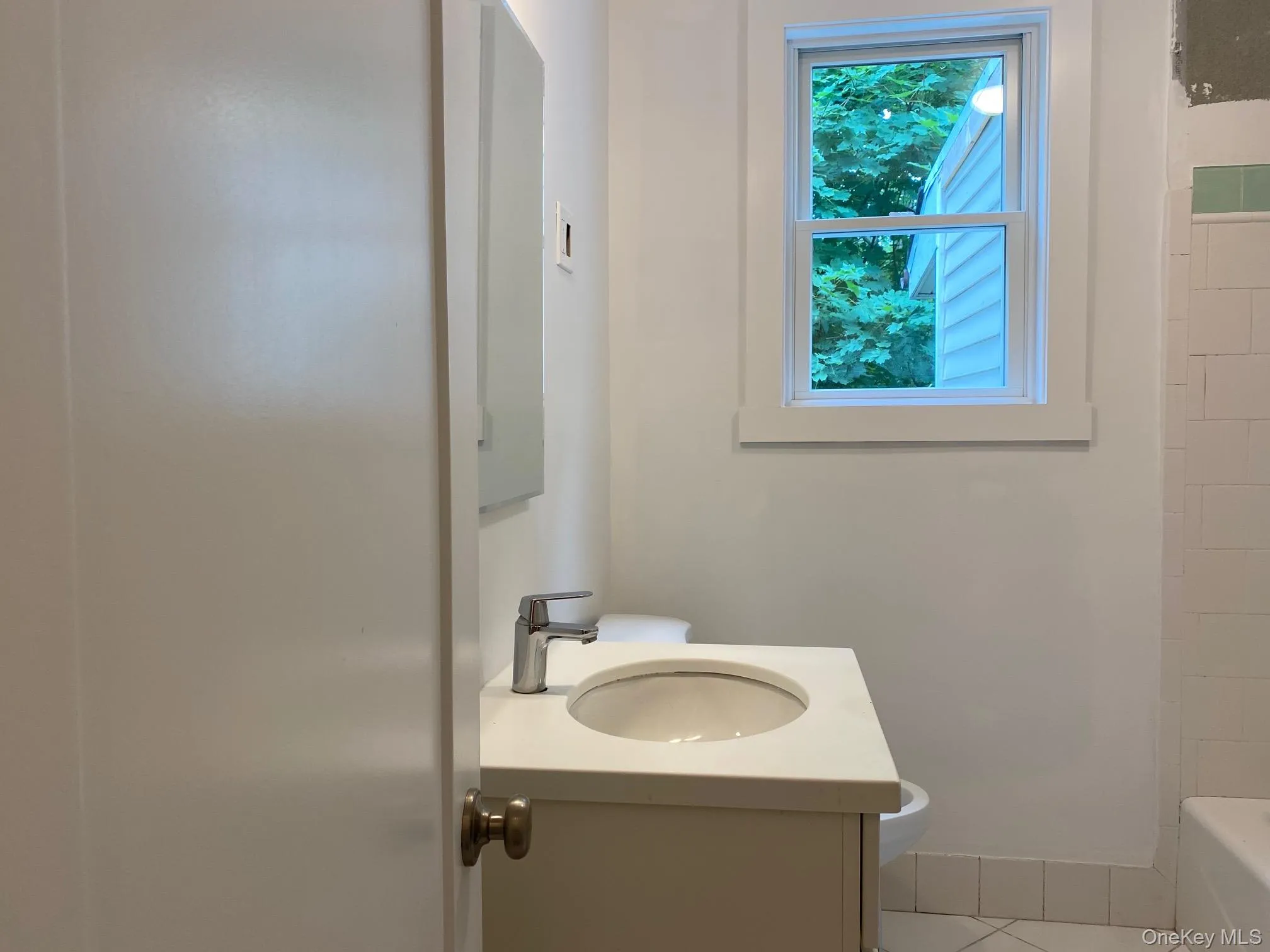 Bathroom featuring a single vanity with an integrated sink and chrome faucet, a framed window, and white wall tiling Bathroom featuring a single vanity with an integrated sink and chrome faucet, a framed window, and white wall tiling