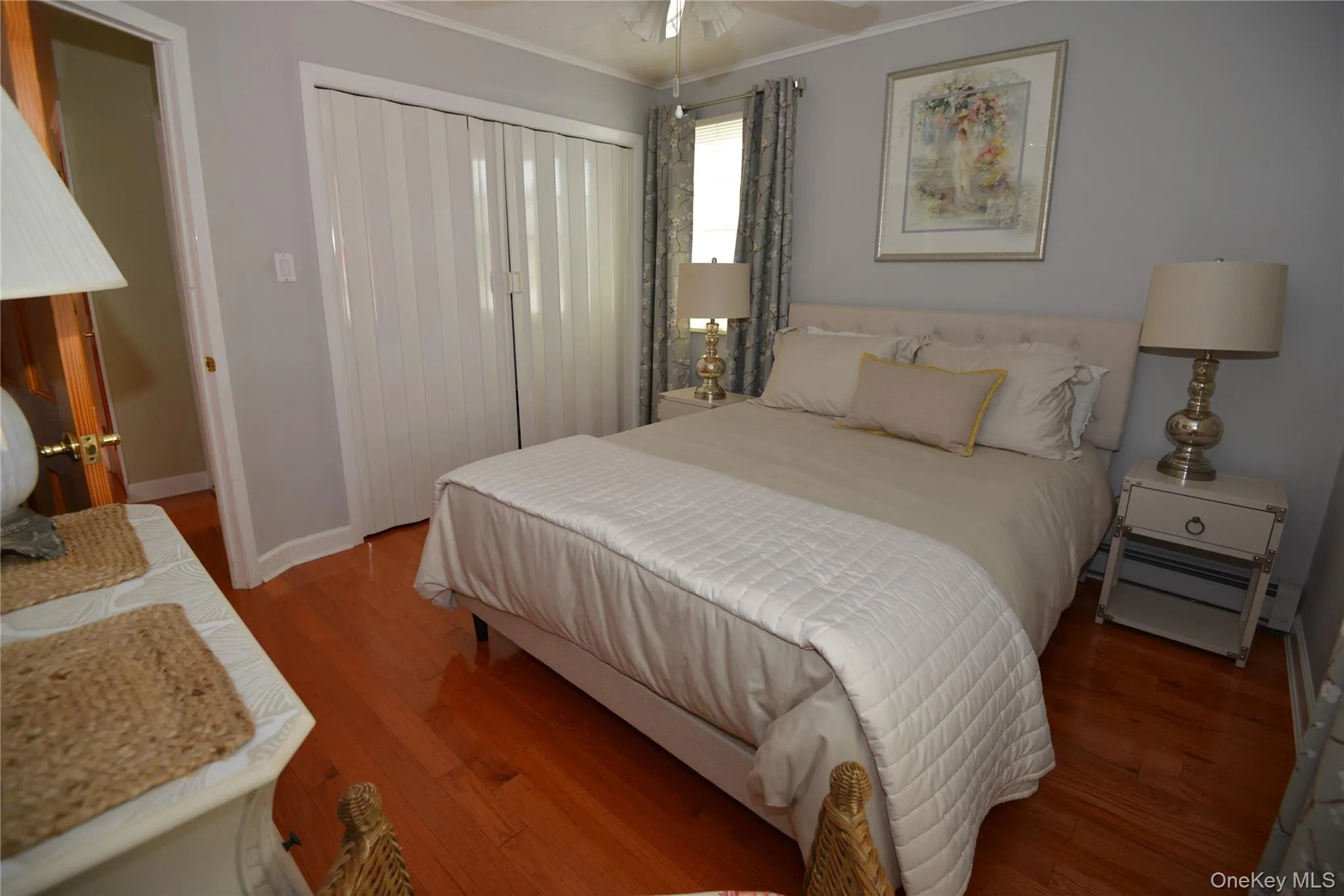 Hardwood-finish flooring highlights this room featuring a built-in closet with bifold doors, light gray wall paint, and white trim Hardwood-finish flooring highlights this room featuring a built-in closet with bifold doors, light gray wall paint, and white trim