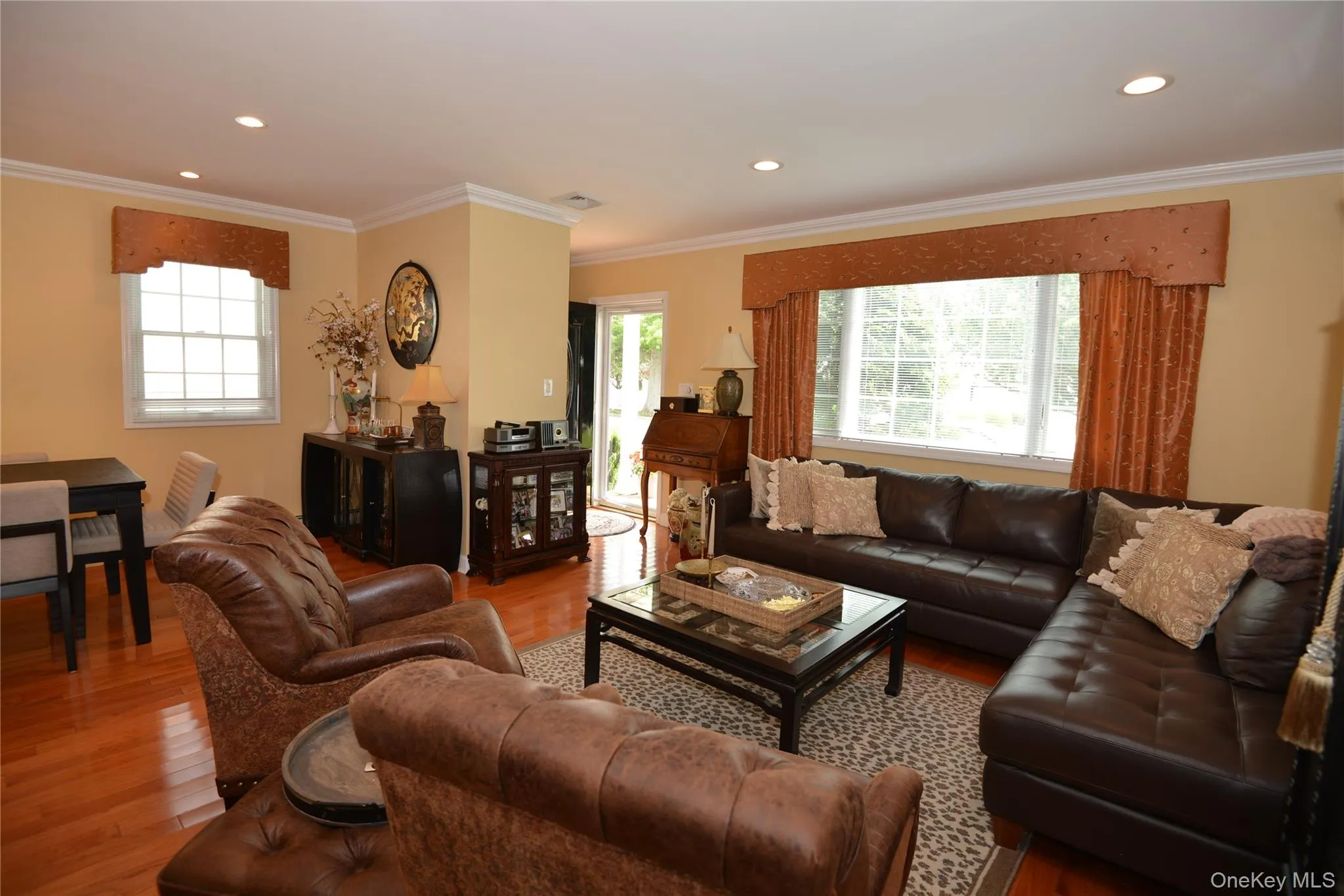 Spacious living area featuring wood-finish flooring, recessed lighting, crown molding, and two multi-pane windows with valances Spacious living area featuring wood-finish flooring, recessed lighting, crown molding, and two multi-pane windows with valances