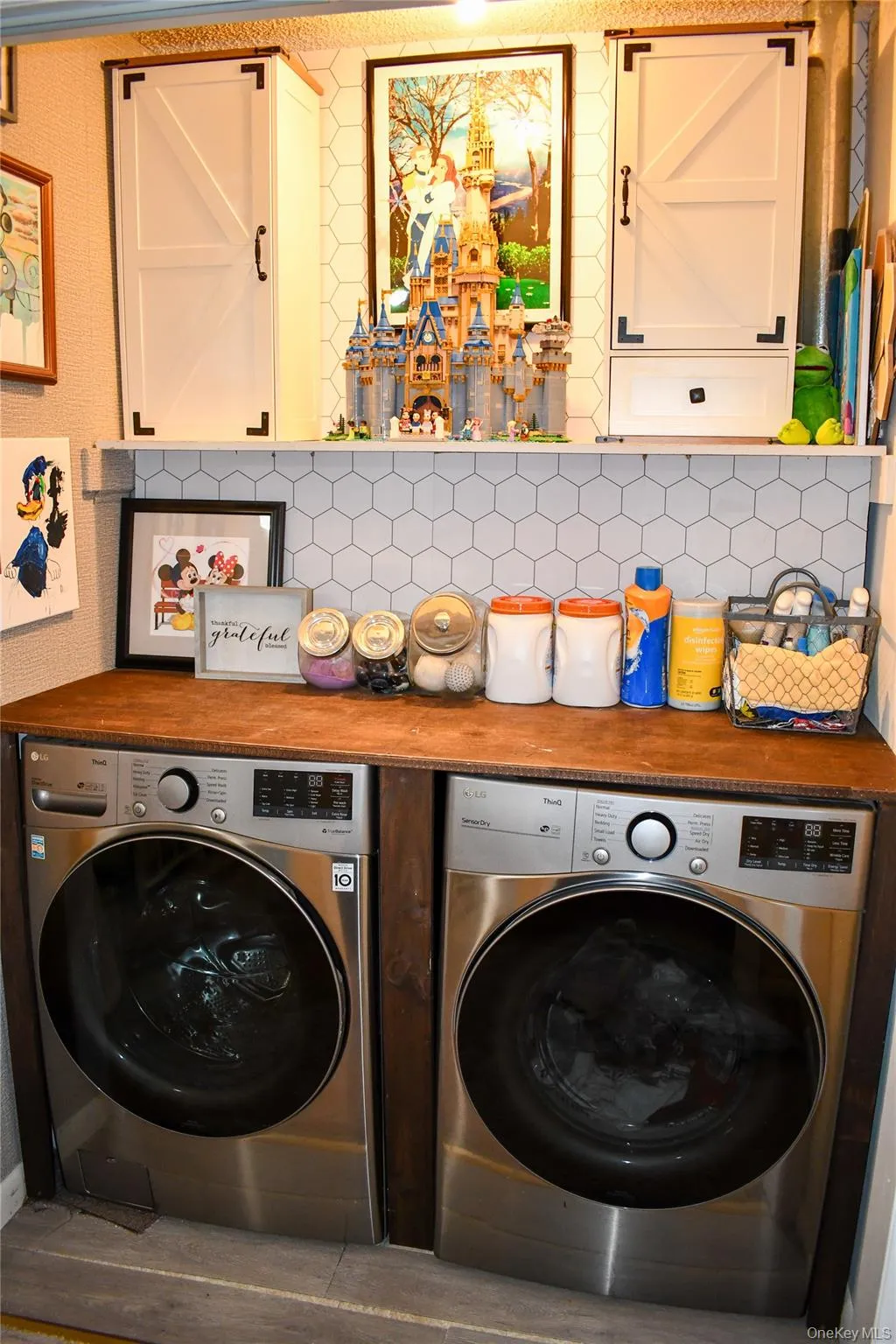 Dedicated laundry area featuring dual stainless steel front-load appliances beneath a wood-finish countertop Dedicated laundry area featuring dual stainless steel front-load appliances beneath a wood-finish countertop