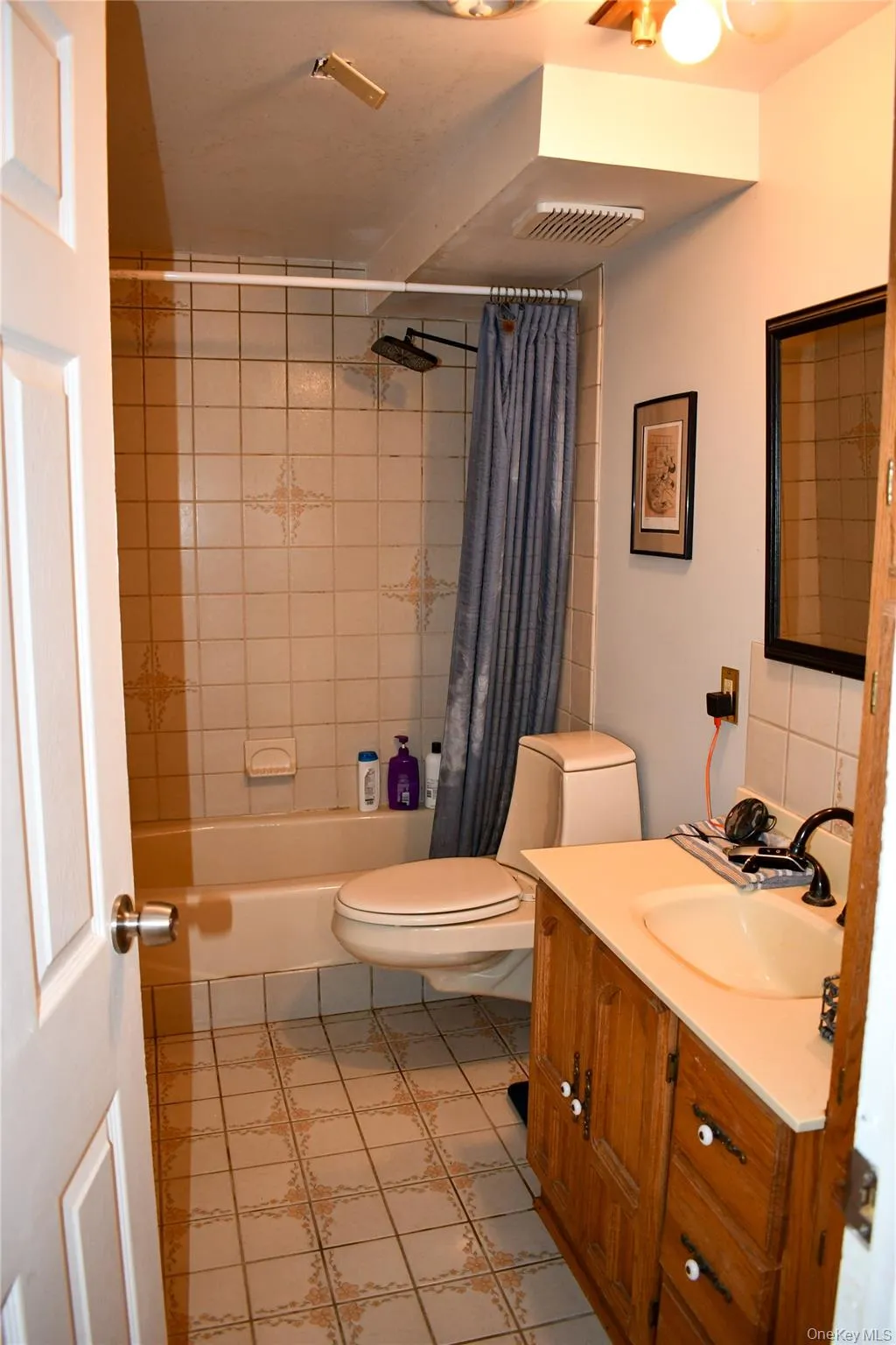 Bathroom featuring a tub/shower combination with tiled surround, a toilet, and a wood-finish vanity with an integrated sink Bathroom featuring a tub/shower combination with tiled surround, a toilet, and a wood-finish vanity with an integrated sink