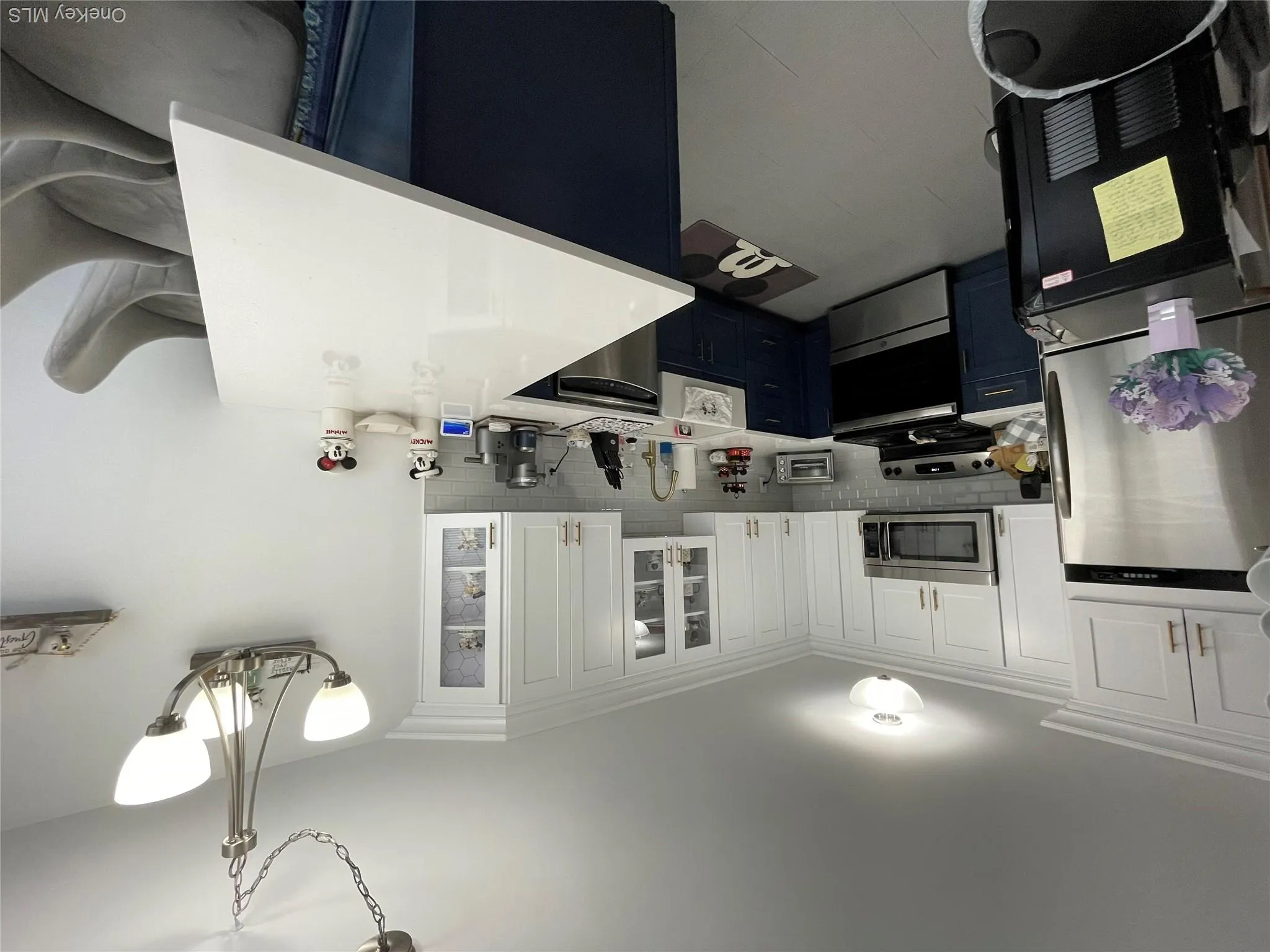 Kitchen featuring two-tone cabinetry with white upper and navy lower cabinets, stainless steel appliances, a white subway tile backsplash, and a peninsula with a light-toned countertop Kitchen featuring two-tone cabinetry with white upper and navy lower cabinets, stainless steel appliances, a white subway tile backsplash, and a peninsula with a light-toned countertop
